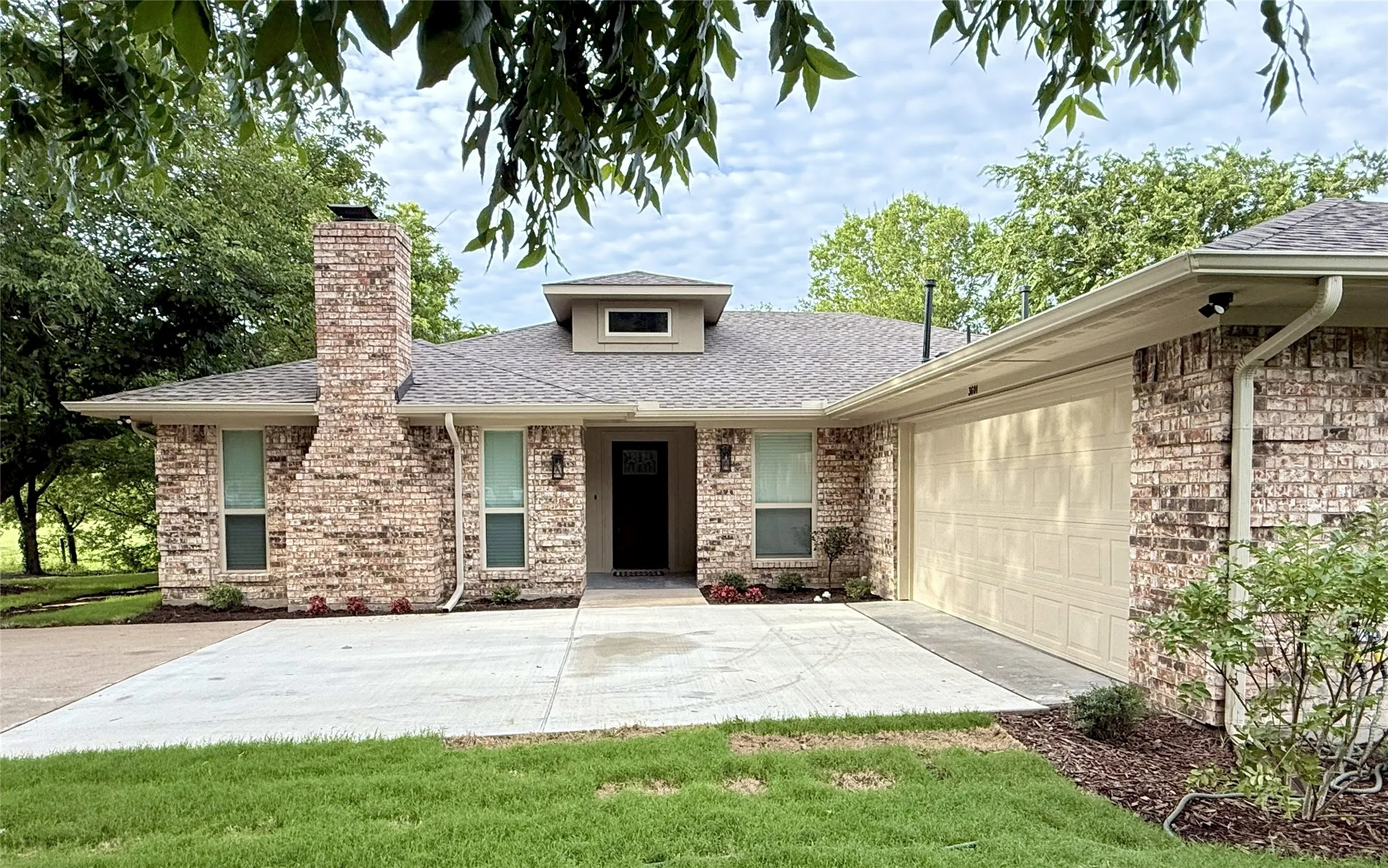 View of front of home with roof with shingles, a chimney, an attached garage, brick siding, and driveway