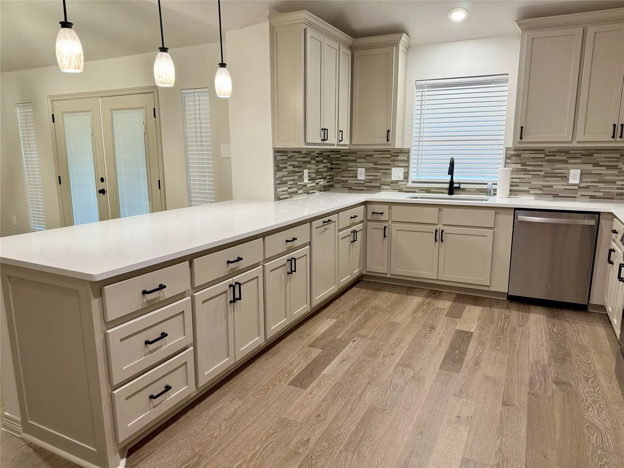 Kitchen with stainless steel dishwasher, a peninsula, light wood-type flooring, tasteful backsplash, and light countertops