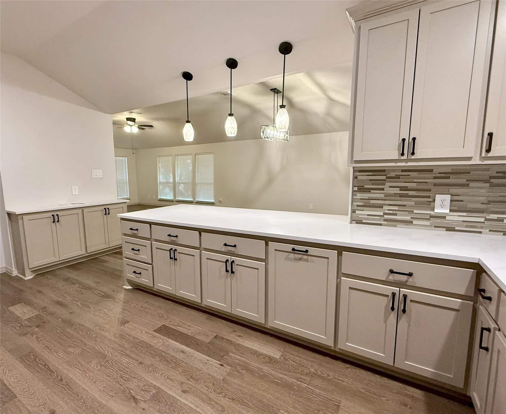 Kitchen with vaulted ceiling, a peninsula, ceiling fan, tasteful backsplash, custom cabinets and pendant lighting