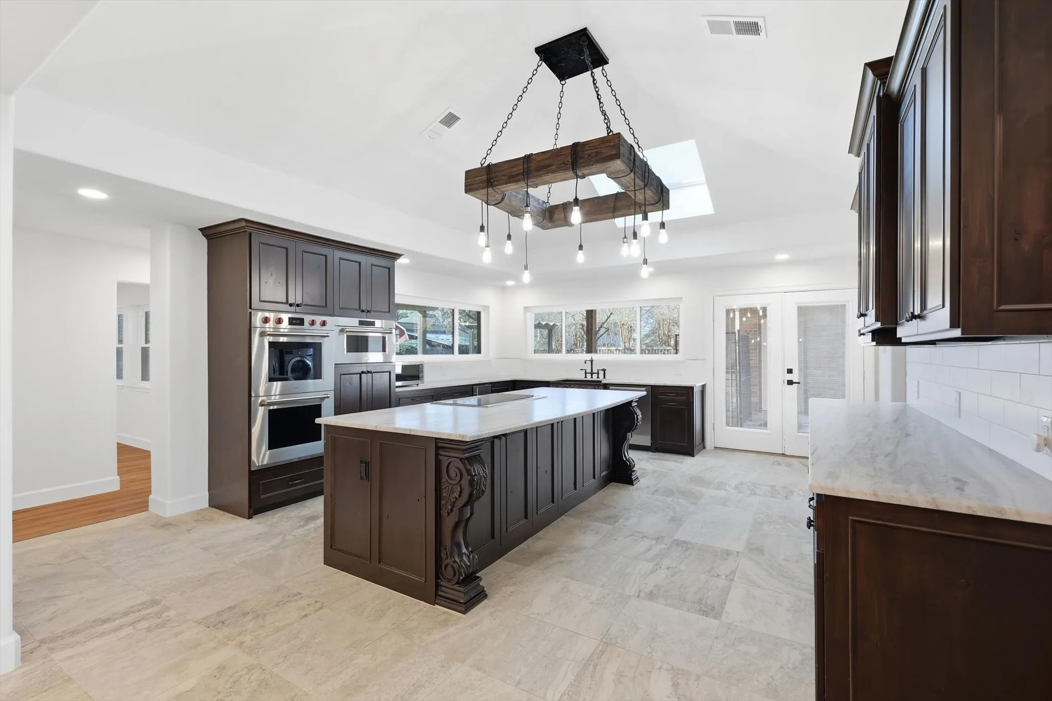 Kitchen with a kitchen island, light stone counters, a skylight, stainless steel appliances, and dark wood finish cabinetry