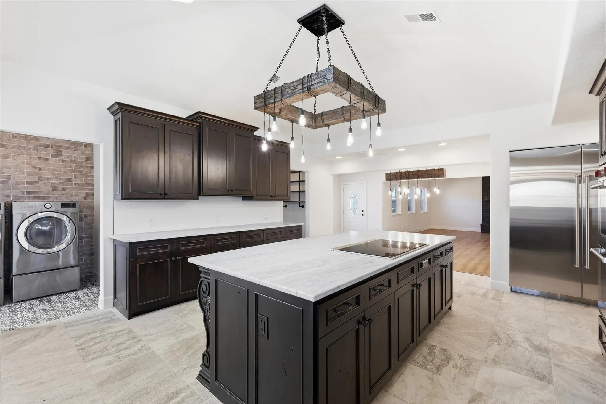 Kitchen featuring a kitchen island, washer / dryer, stainless steel built in refrigerator, dark wood finish cabinetry, and light stone countertops
