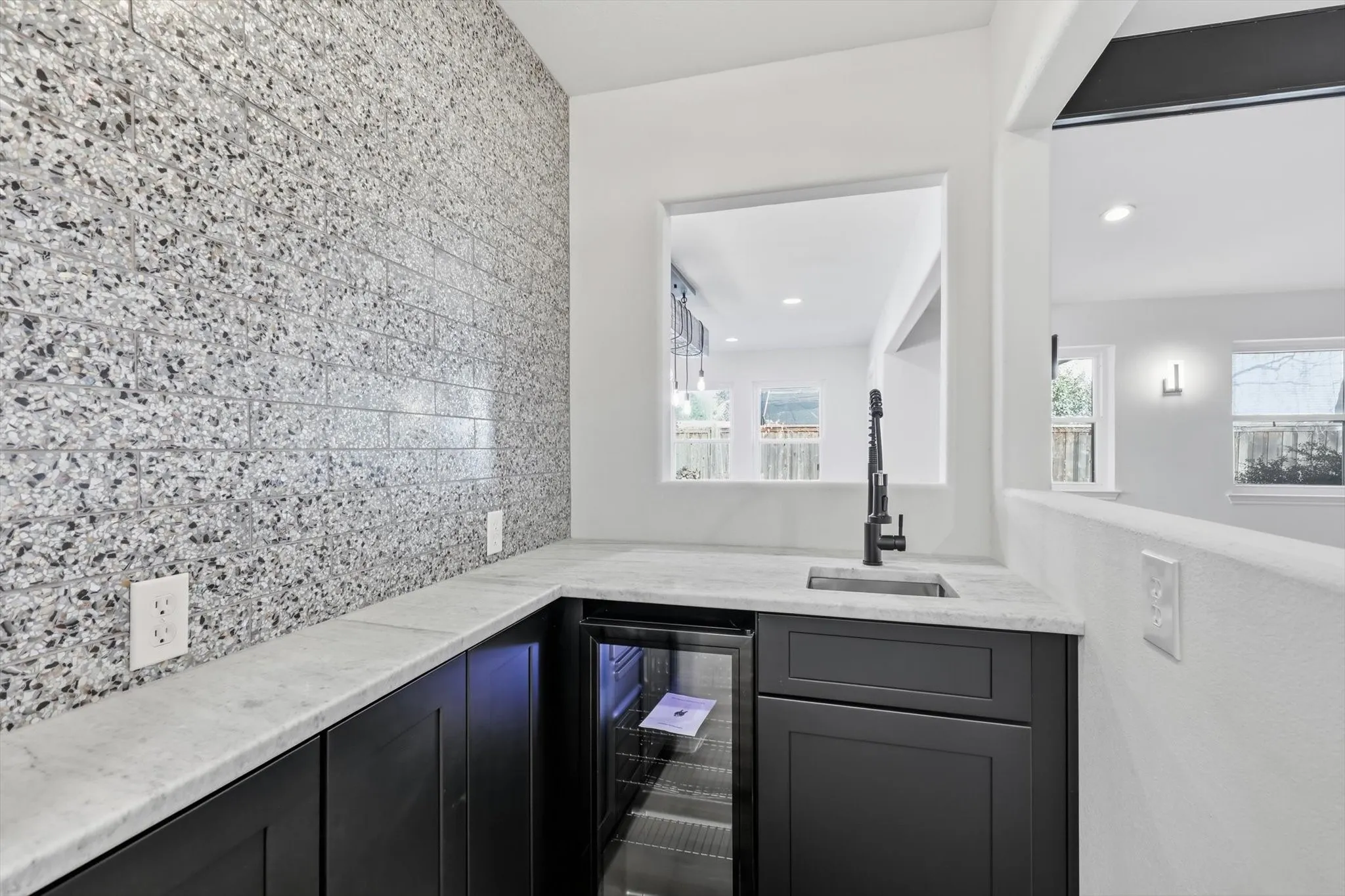 Indoor wet bar featuring beverage cooler, tasteful backsplash, light stone counters, and dark cabinets