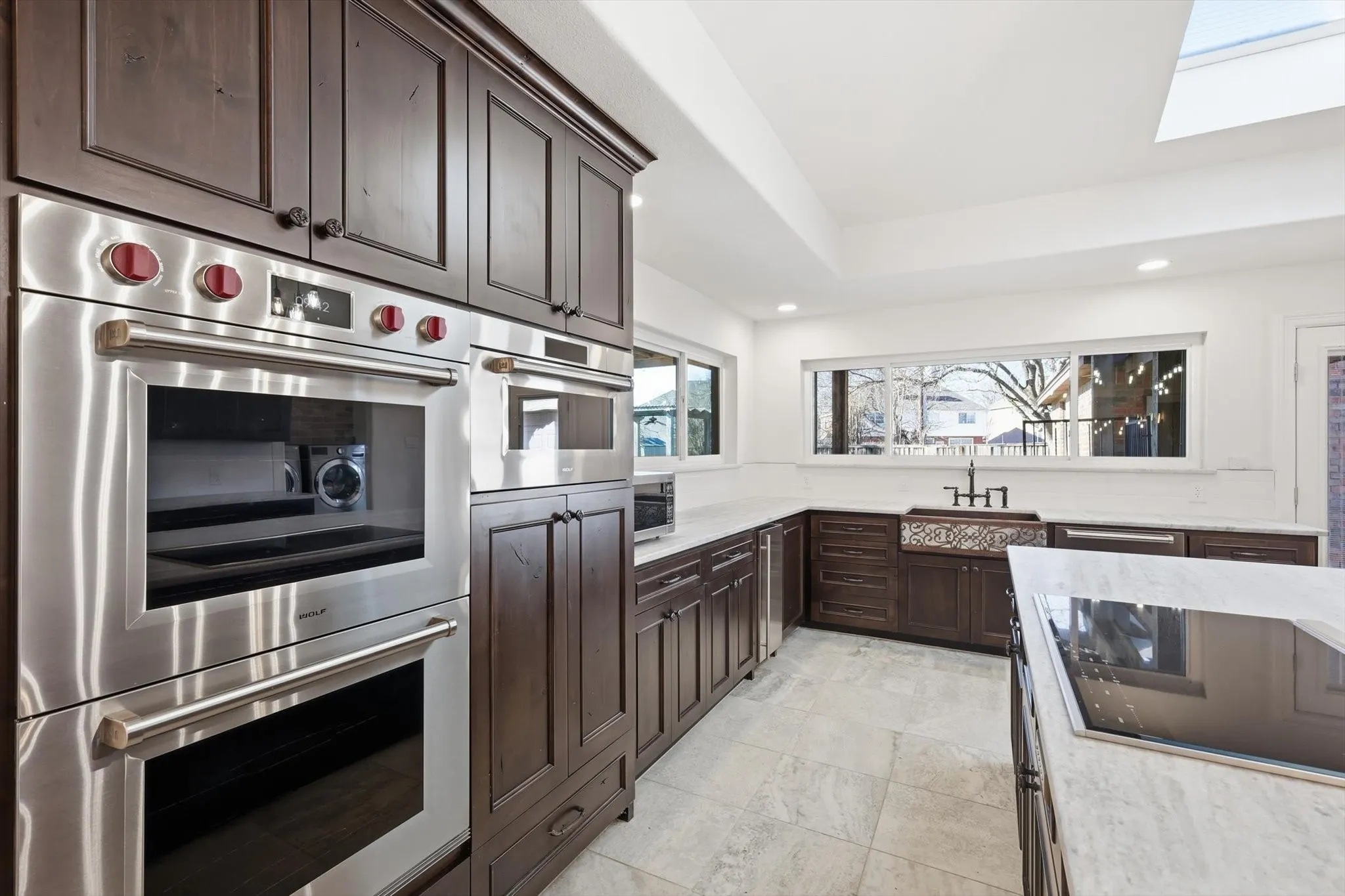 Kitchen featuring stainless steel appliances, dark wood finish cabinetry, a skylight, recessed lighting, and light stone countertops