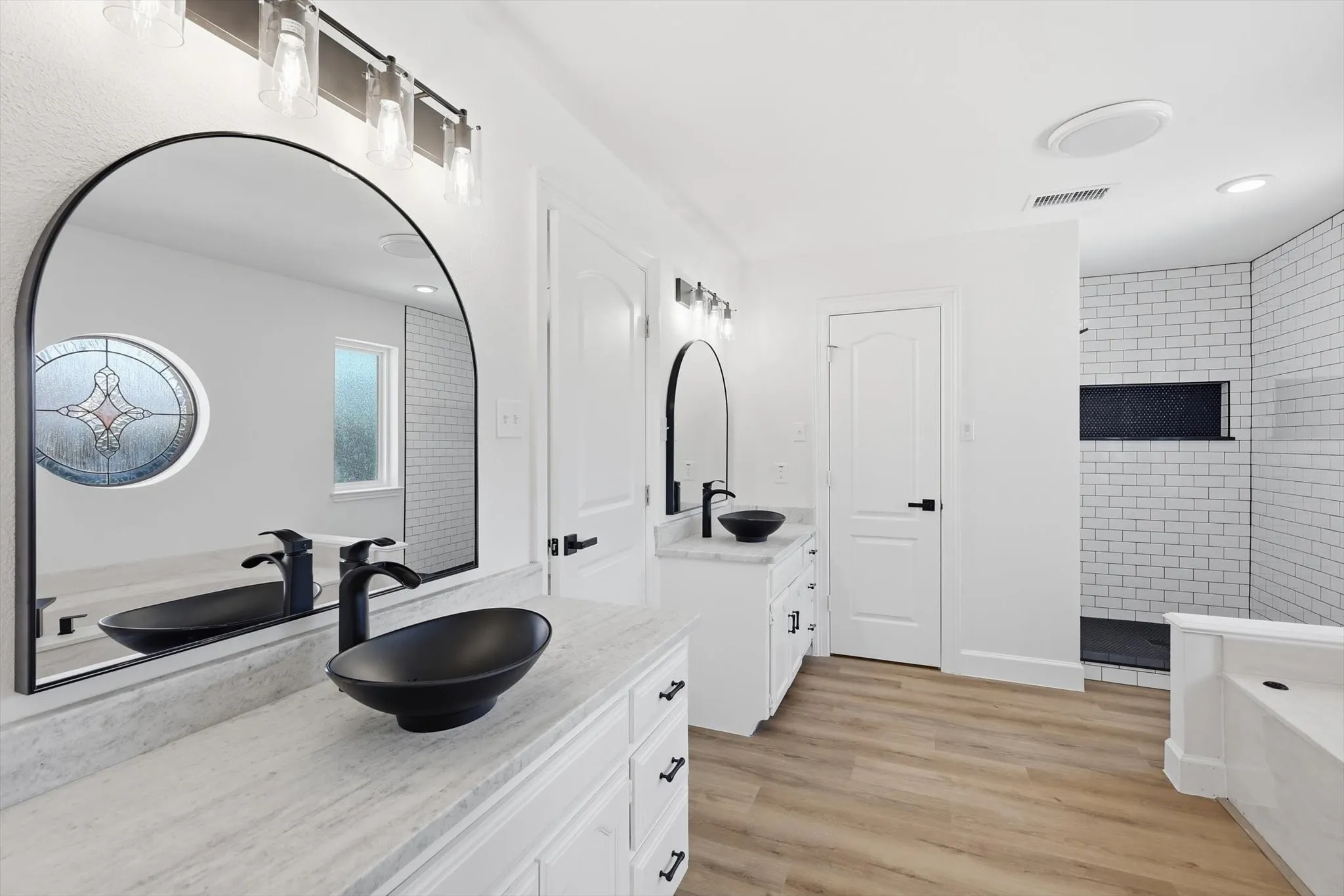 Full bathroom featuring two vanities, a bathtub, light wood-style flooring, tiled shower, and recessed lighting