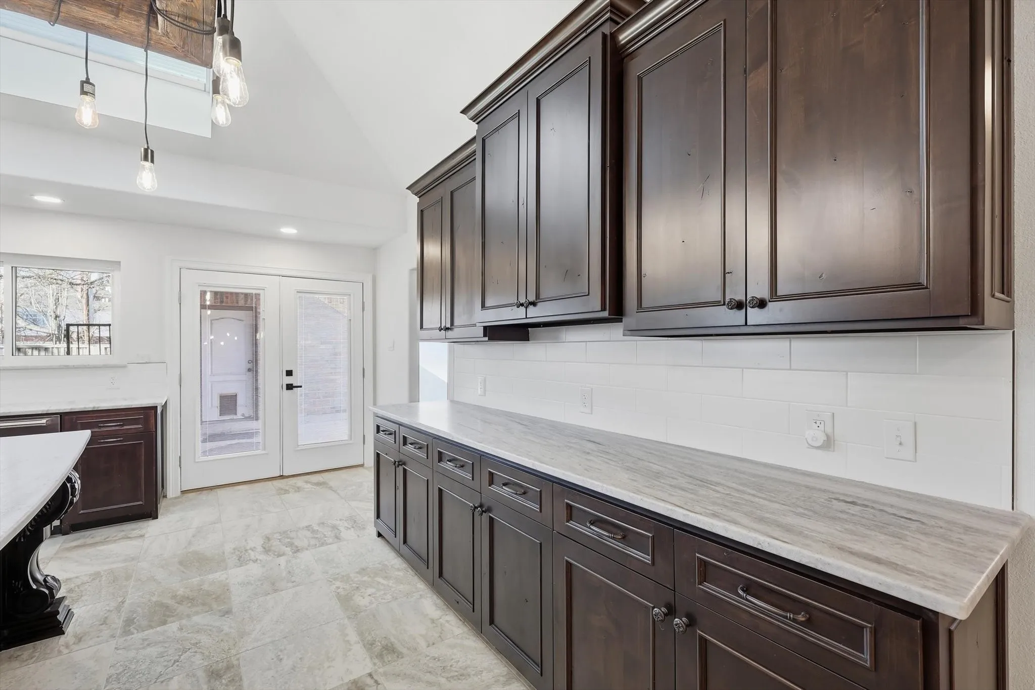 Kitchen with dark wood finish cabinets, french doors, vaulted ceiling, and light stone countertops