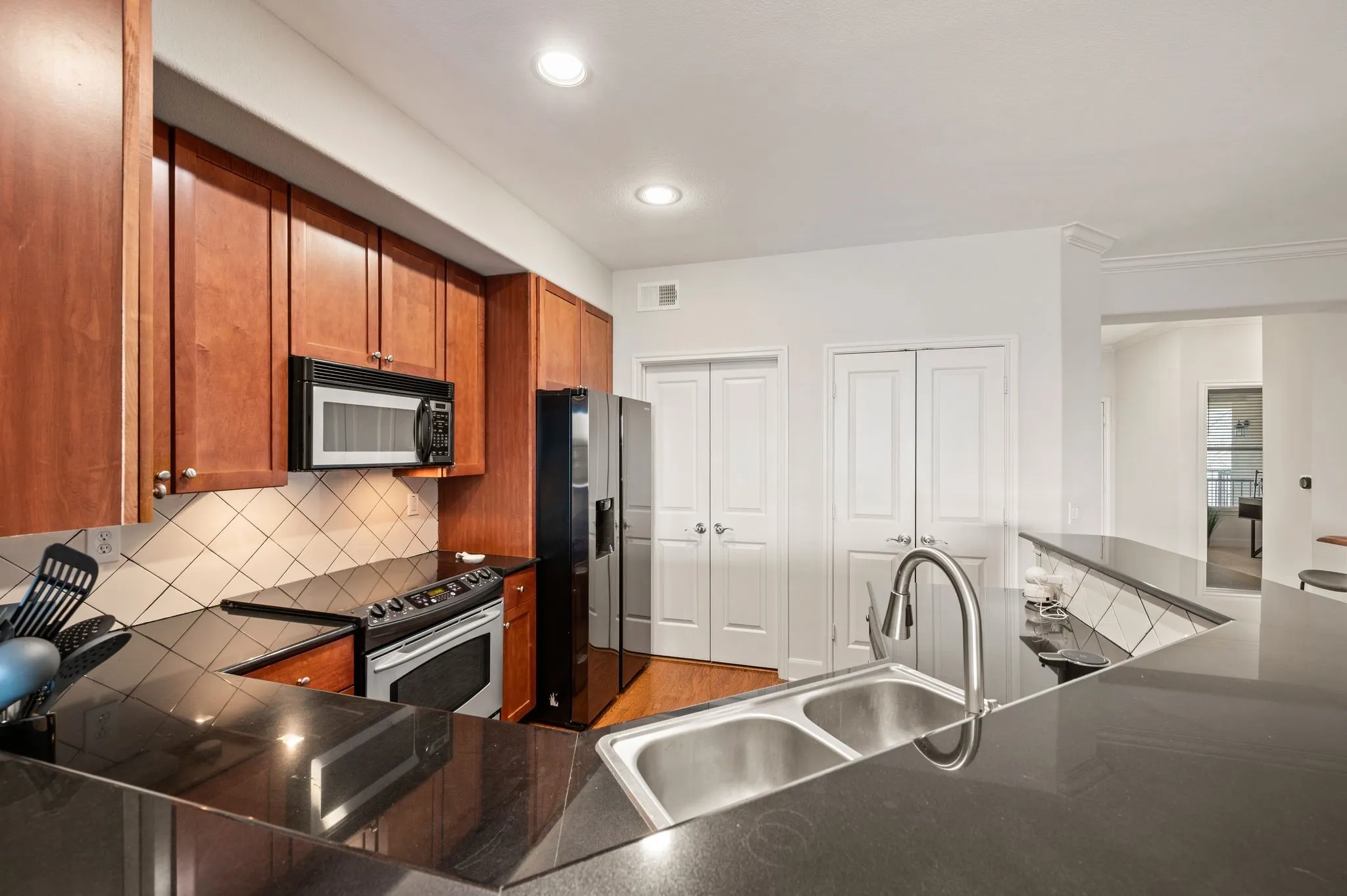 Kitchen with wood finish cabinets, dark countertops, black appliances, backsplash, and recessed lighting