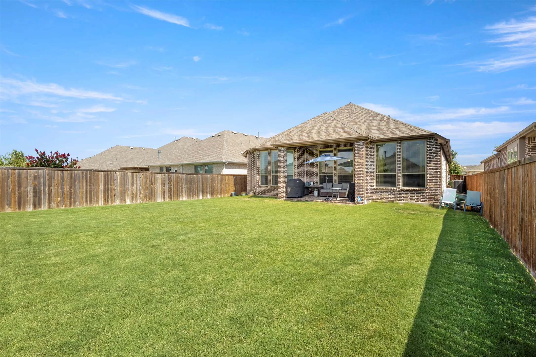 Rear view of property featuring brick siding, a fenced backyard, and a patio area