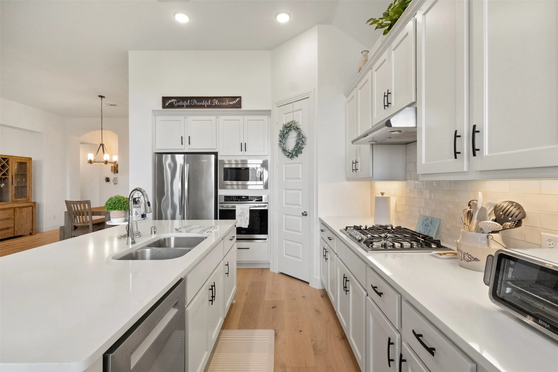 Kitchen with appliances with stainless steel finishes, under cabinet range hood, a chandelier, white cabinets, and recessed lighting