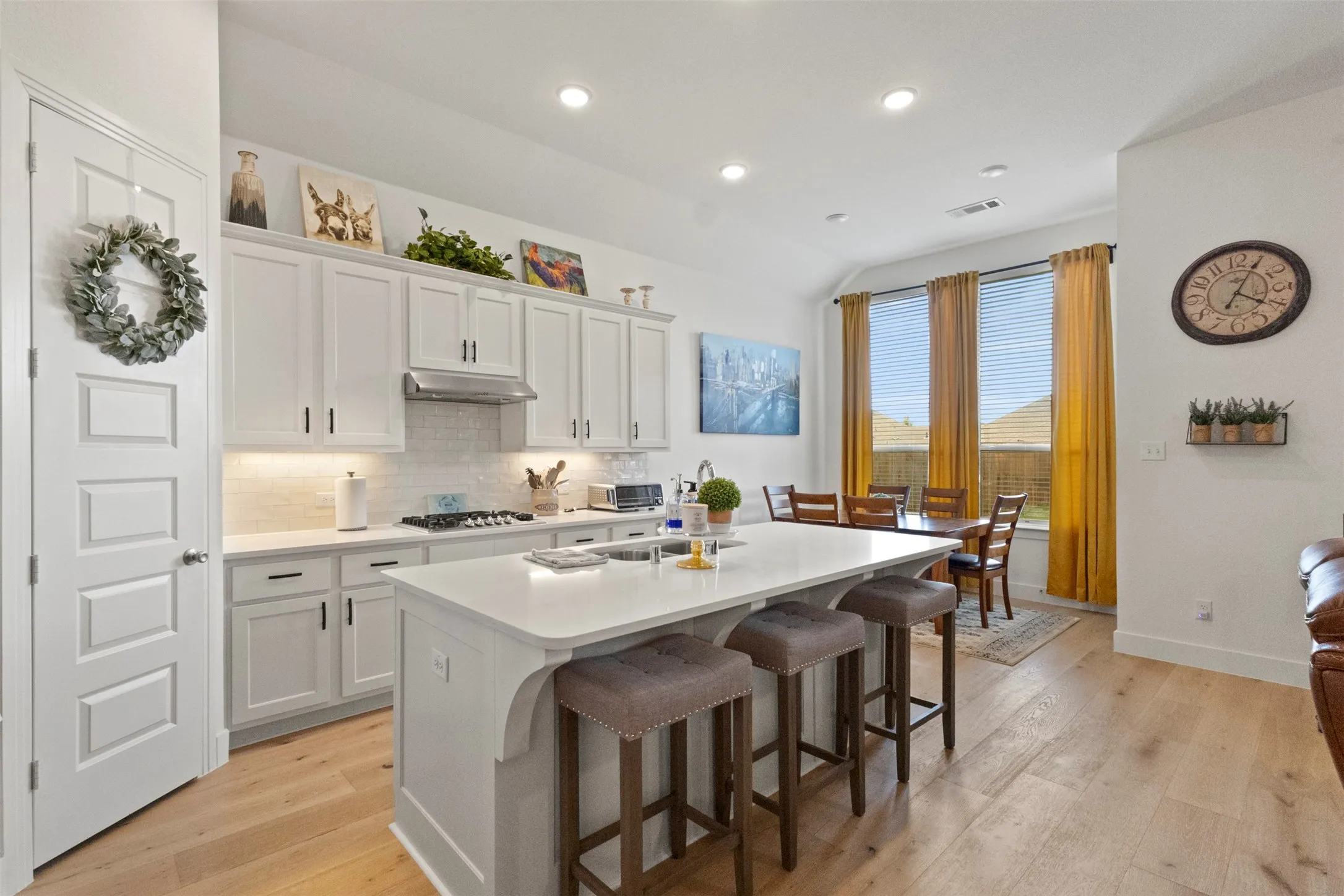 Kitchen with under cabinet range hood, a center island with sink, light wood finished floors, tasteful backsplash, and stainless steel gas cooktop