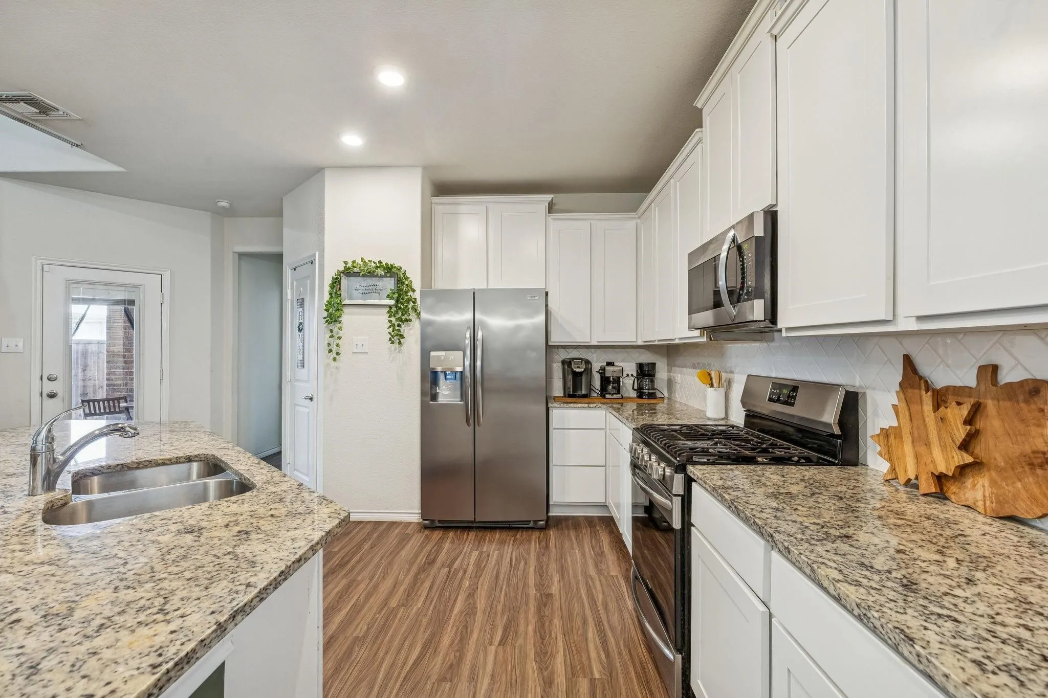 Kitchen featuring wood-finish flooring, white cabinetry, granite countertops, stainless steel appliances, and an undermount double sink