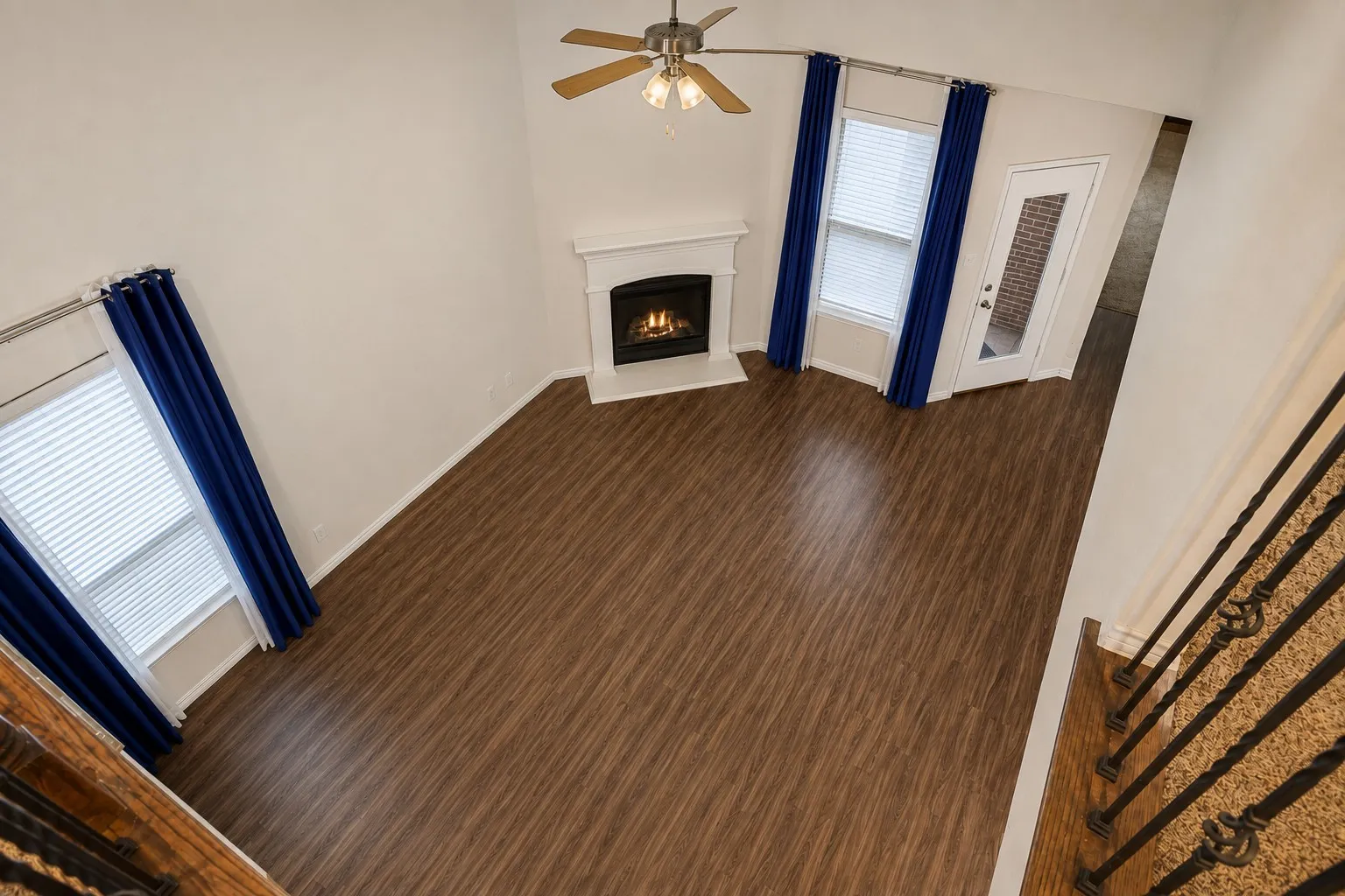 Vaulted ceiling with a ceiling fan, fireplace with a white mantel, wood-finish flooring, and multiple windows with blinds *digitally altered to show potential.*