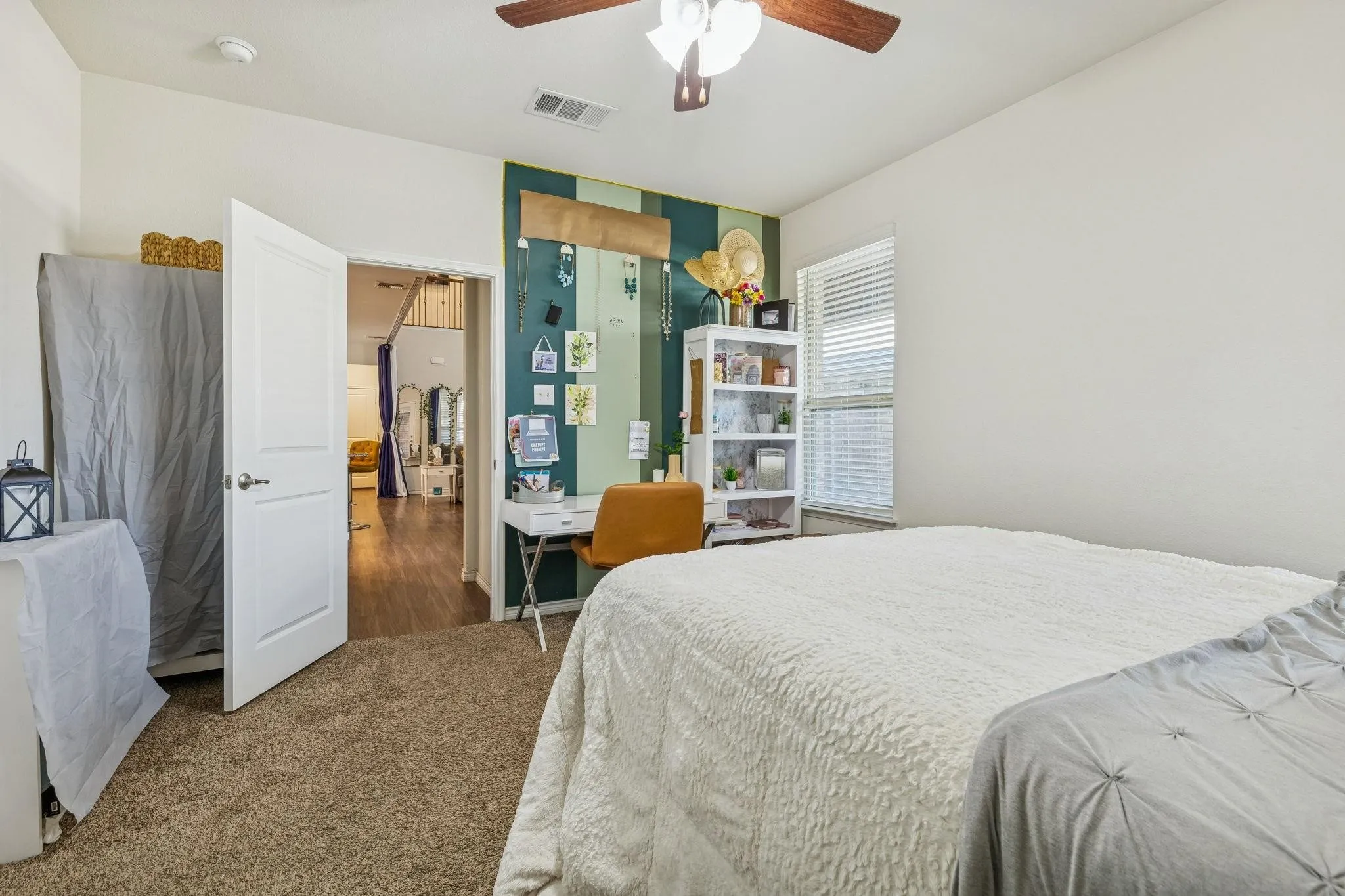 Carpeted room featuring a ceiling fan, a window with blinds, and an open doorway revealing wood-finish flooring