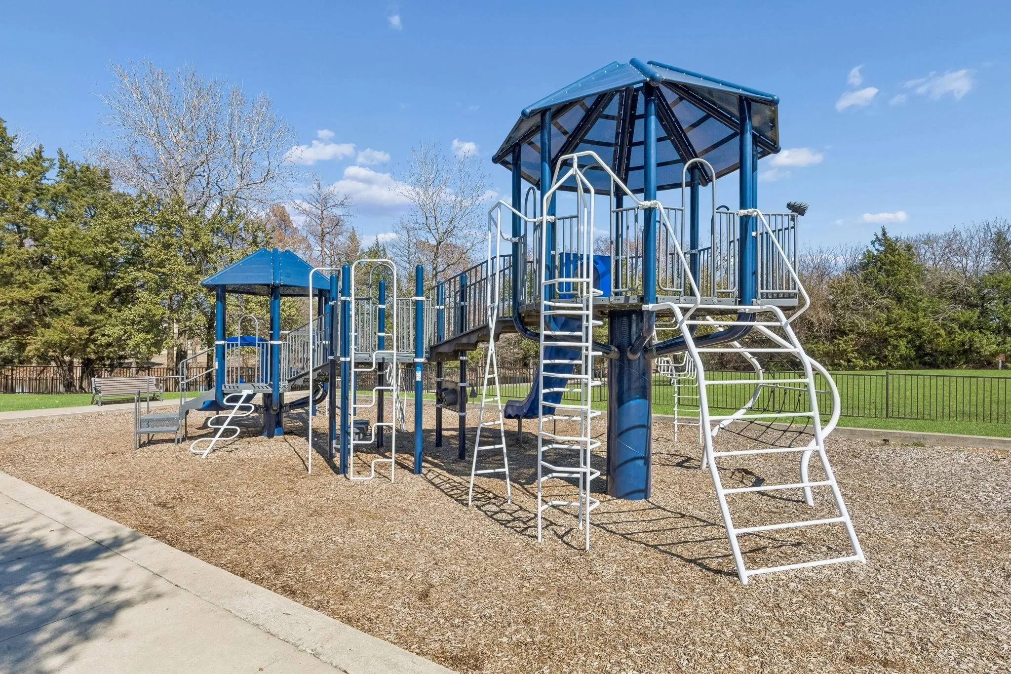 Expansive outdoor playground featuring a multi-level structure with blue and white accents, multiple slides, climbing elements, and a covered platform