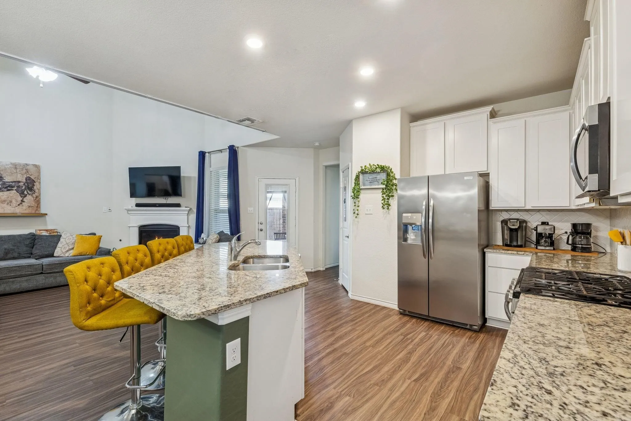 Open-concept kitchen and living area featuring wood-finish flooring, a kitchen island with a granite-style countertop, white cabinetry, and stainless steel appliances