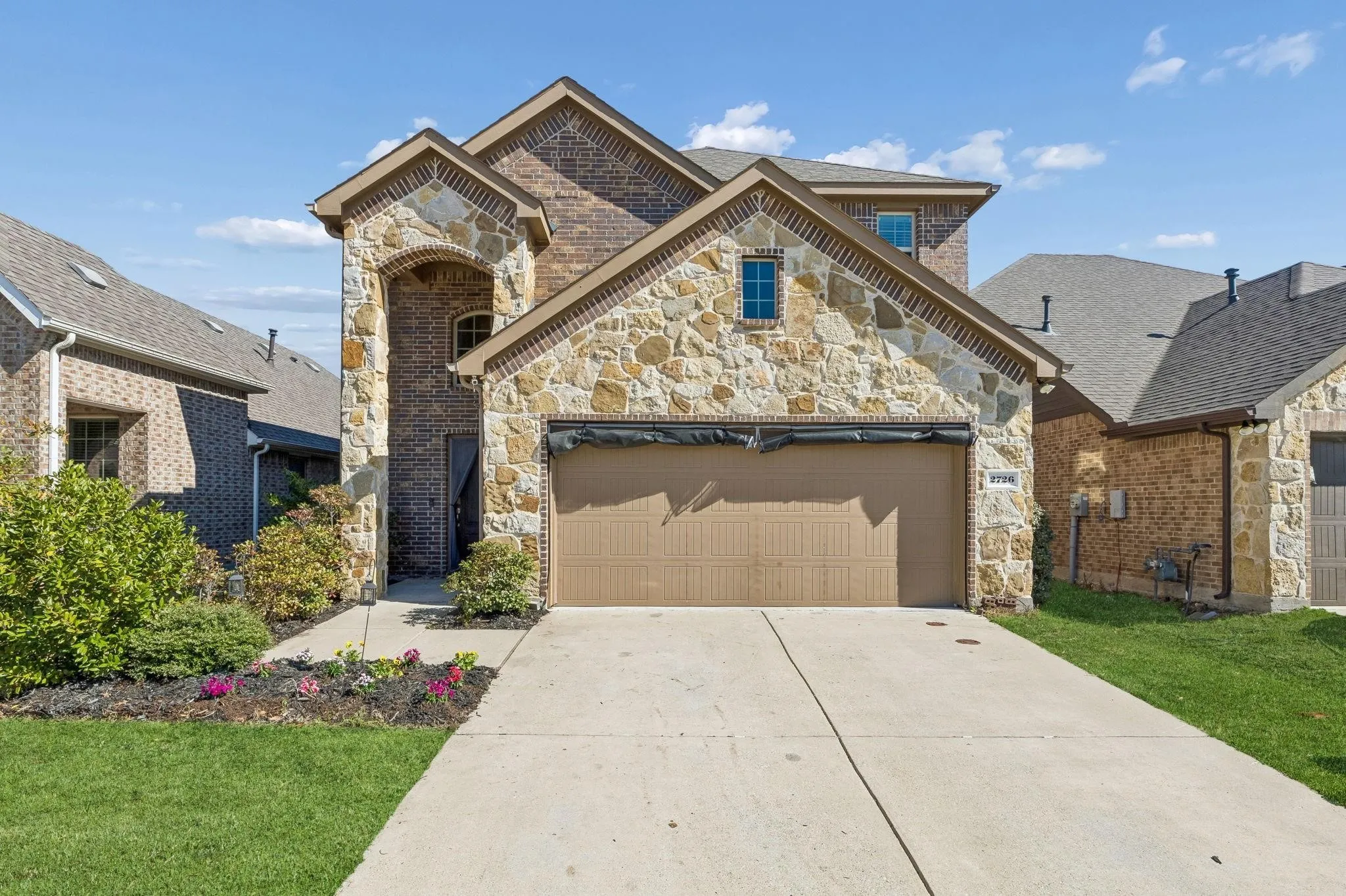 Two-story residence featuring a brick and stone facade, arched entryway, and an attached two-car garage