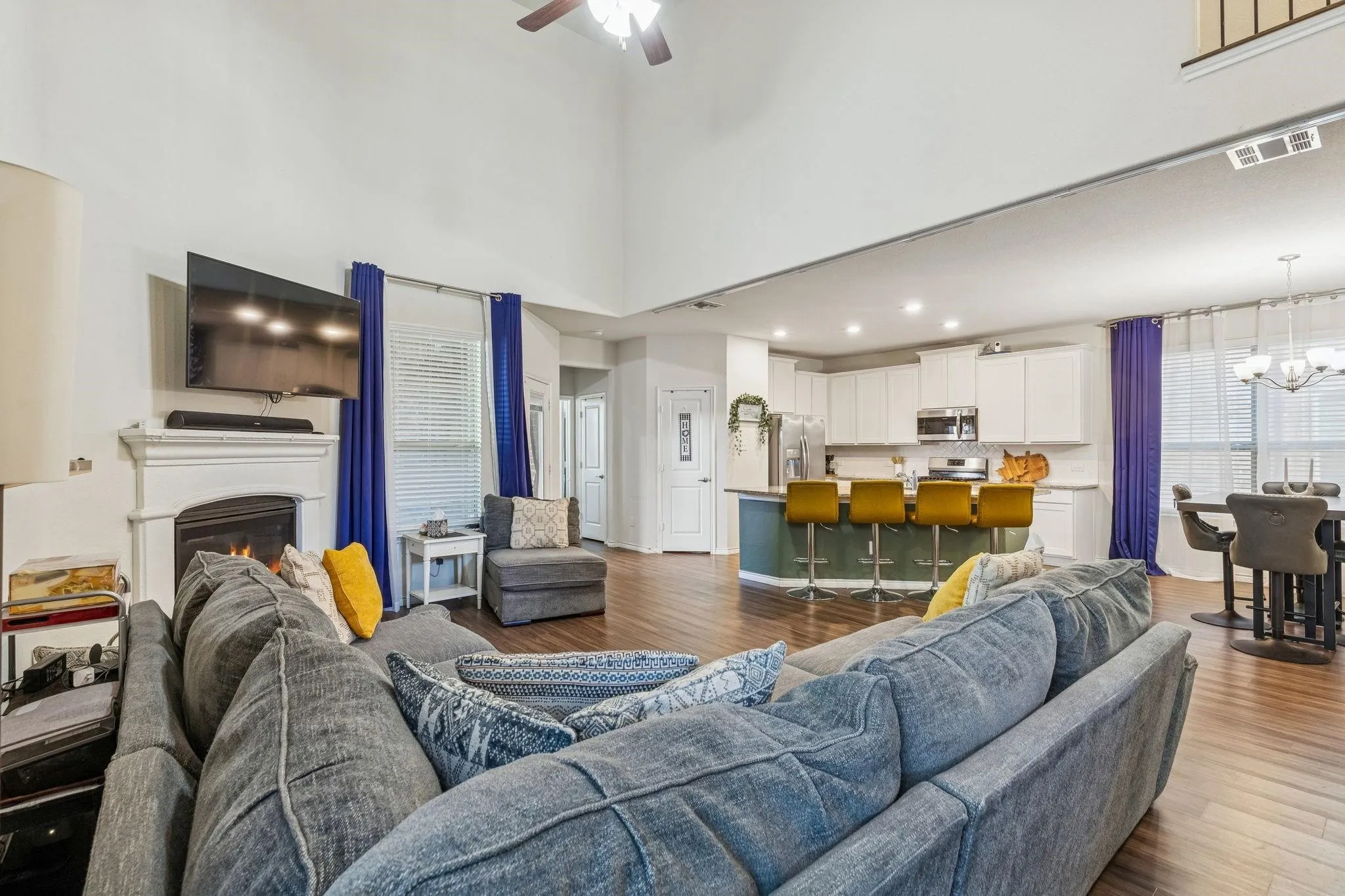 Spacious living area featuring a fireplace with a white mantel, high ceilings, and wood-finish flooring throughout