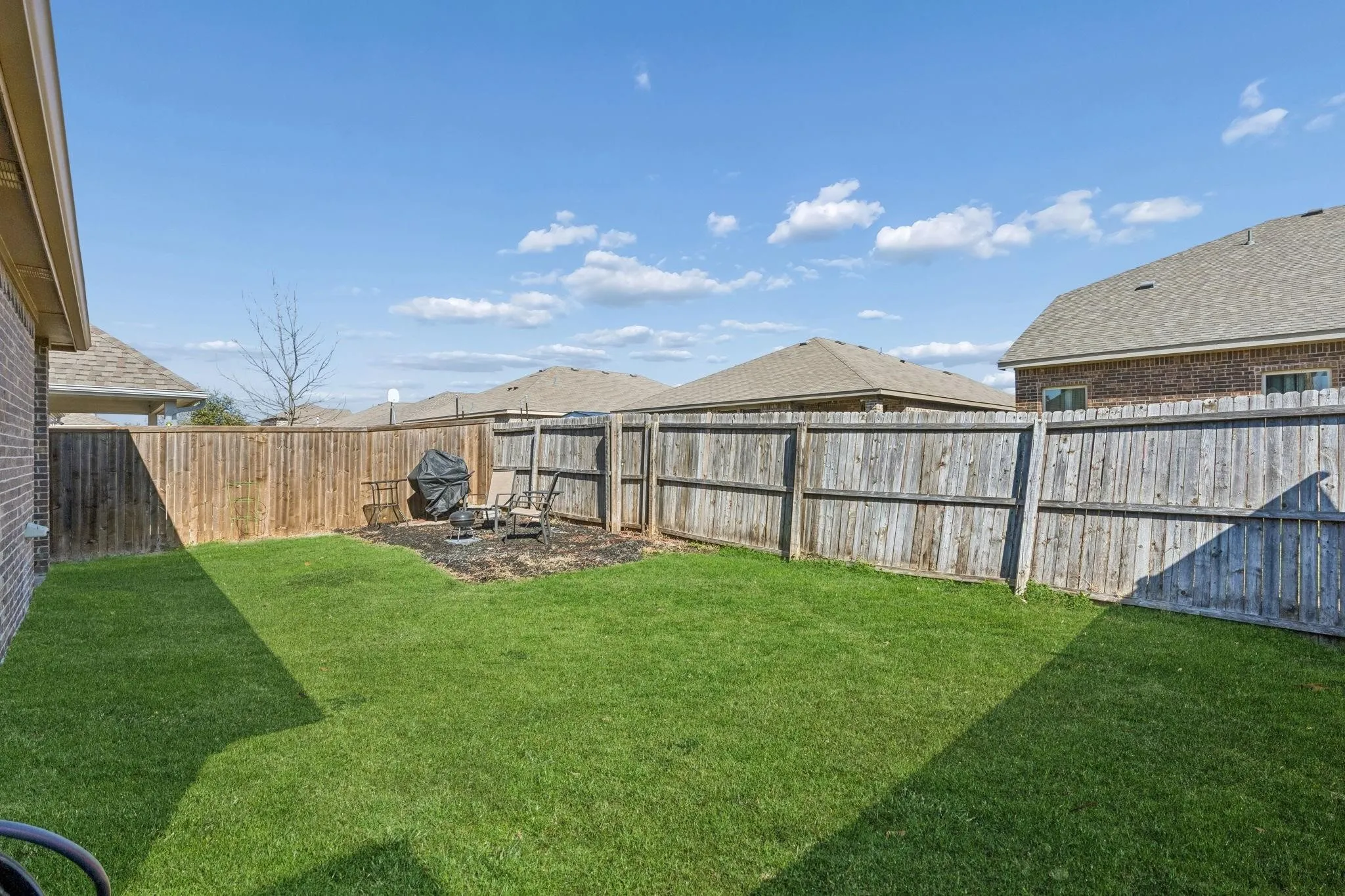 Expansive backyard featuring a manicured lawn, full wood privacy fencing, and a dedicated mulched area