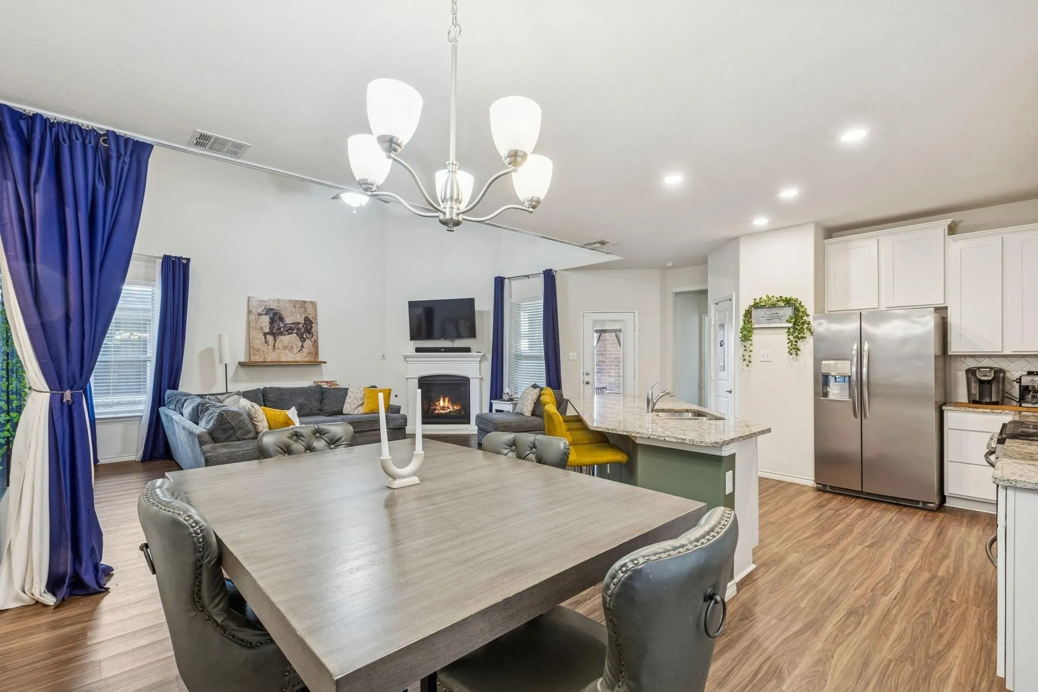 Open-concept living space featuring wood-finish flooring, a fireplace with a white mantel, and a kitchen island with a granite countertop