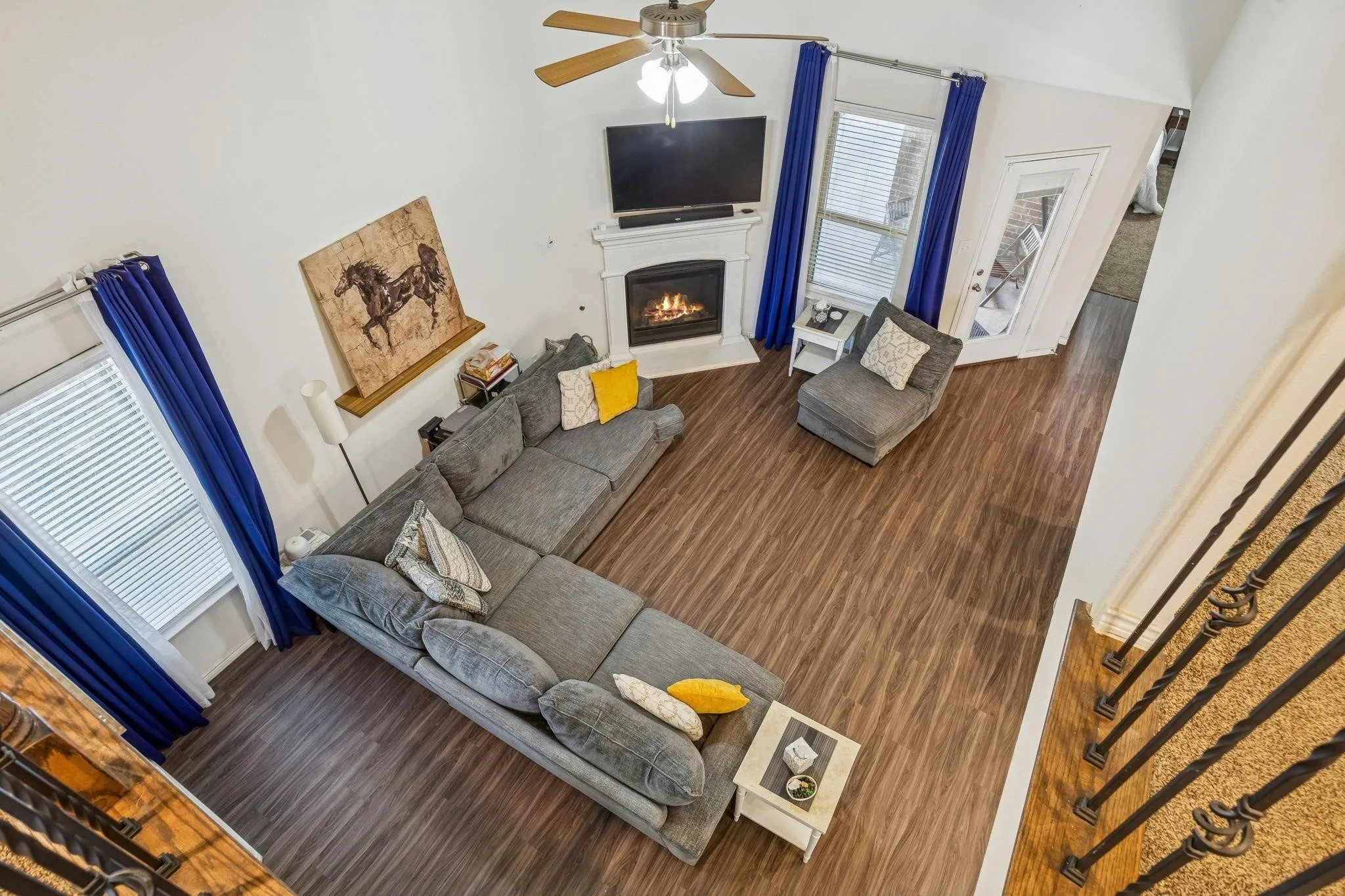 Living room featuring wood-finish flooring, a fireplace with a white mantel, and a ceiling fan