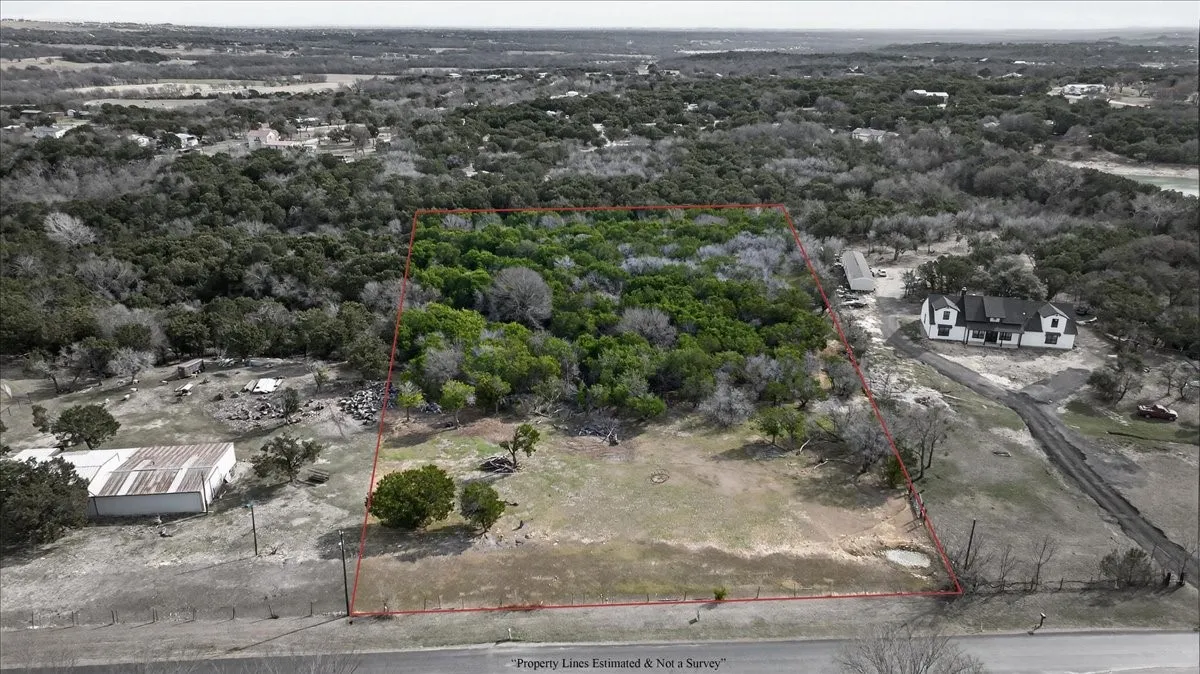 Aerial view of property and surrounding area with property parcel outlined and a heavily wooded area