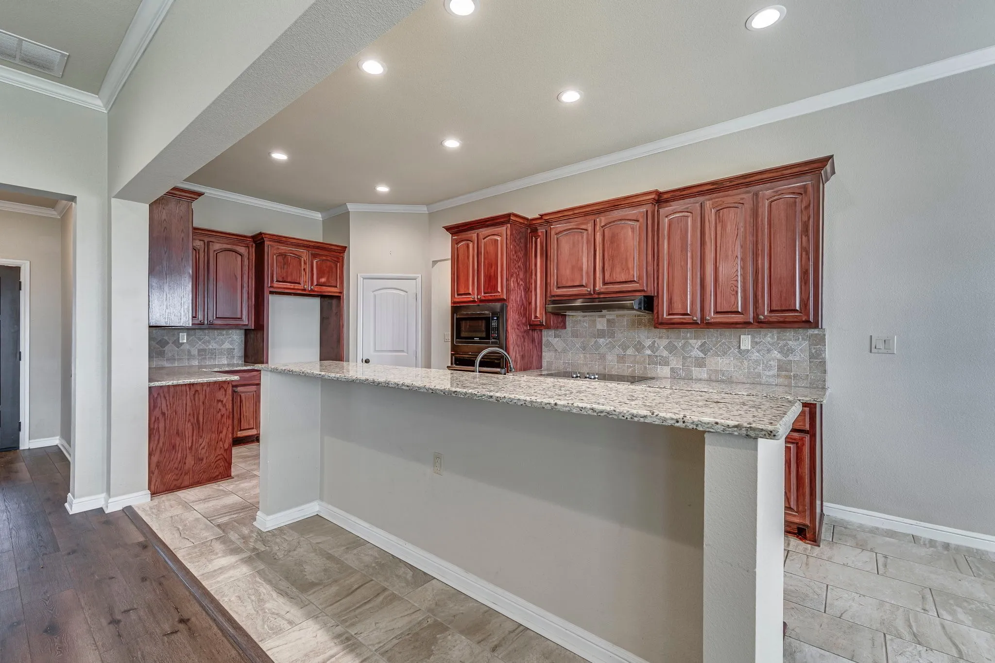 Kitchen featuring decorative backsplash, light stone countertops, crown molding, bold wood finish cabinets, and built in microwave