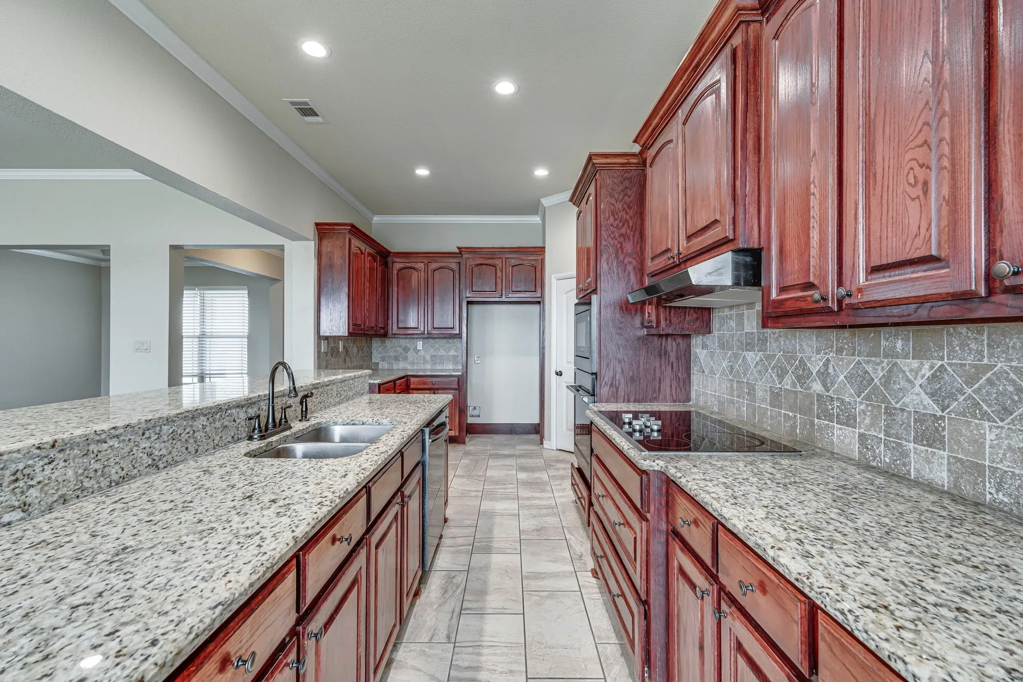 Kitchen featuring light stone counters, decorative backsplash, recessed lighting, ornamental molding, and bold wood finish cabinets