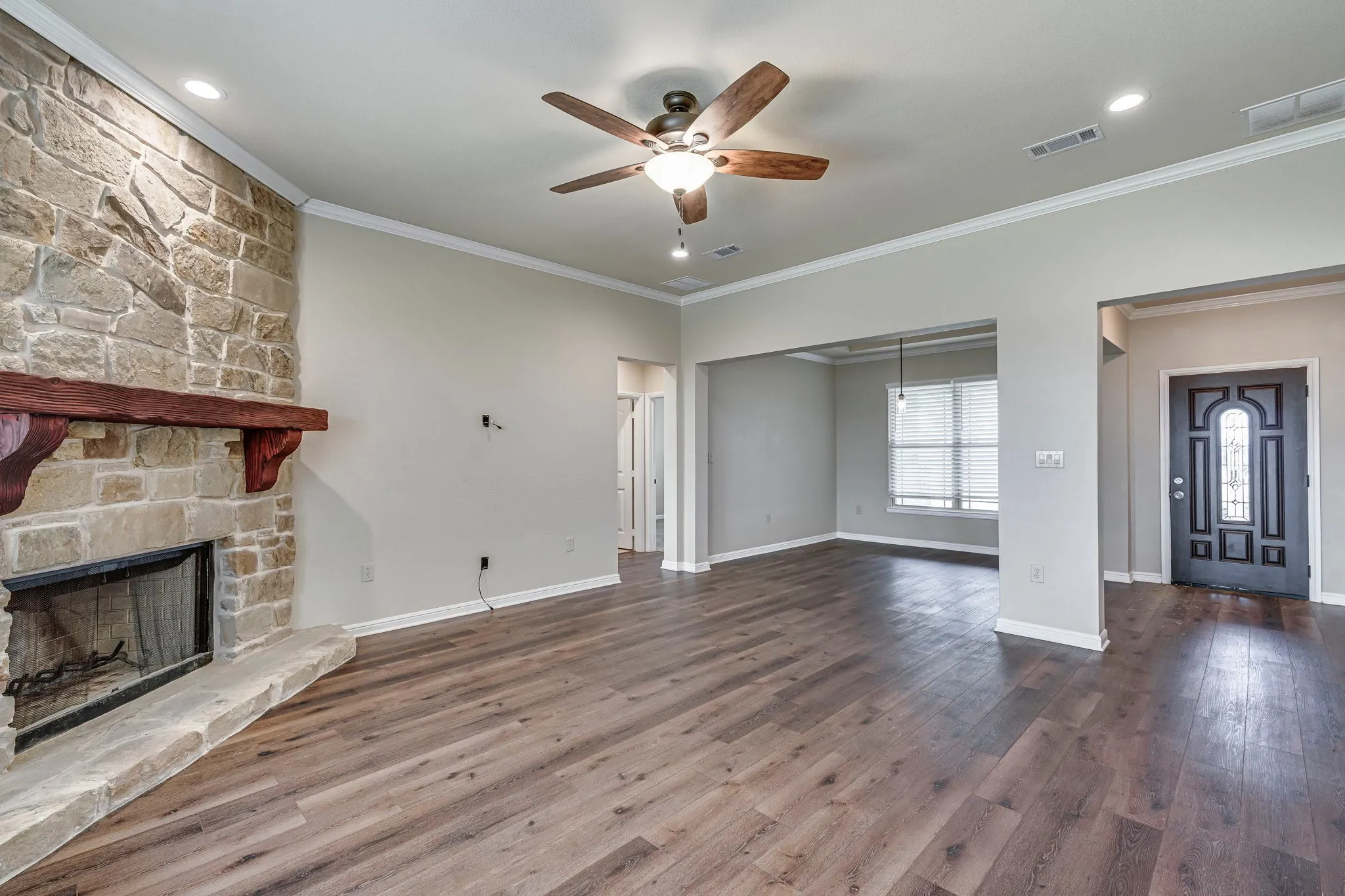 Unfurnished living room with a stone fireplace, a ceiling fan, dark wood finished floors, and ornamental molding