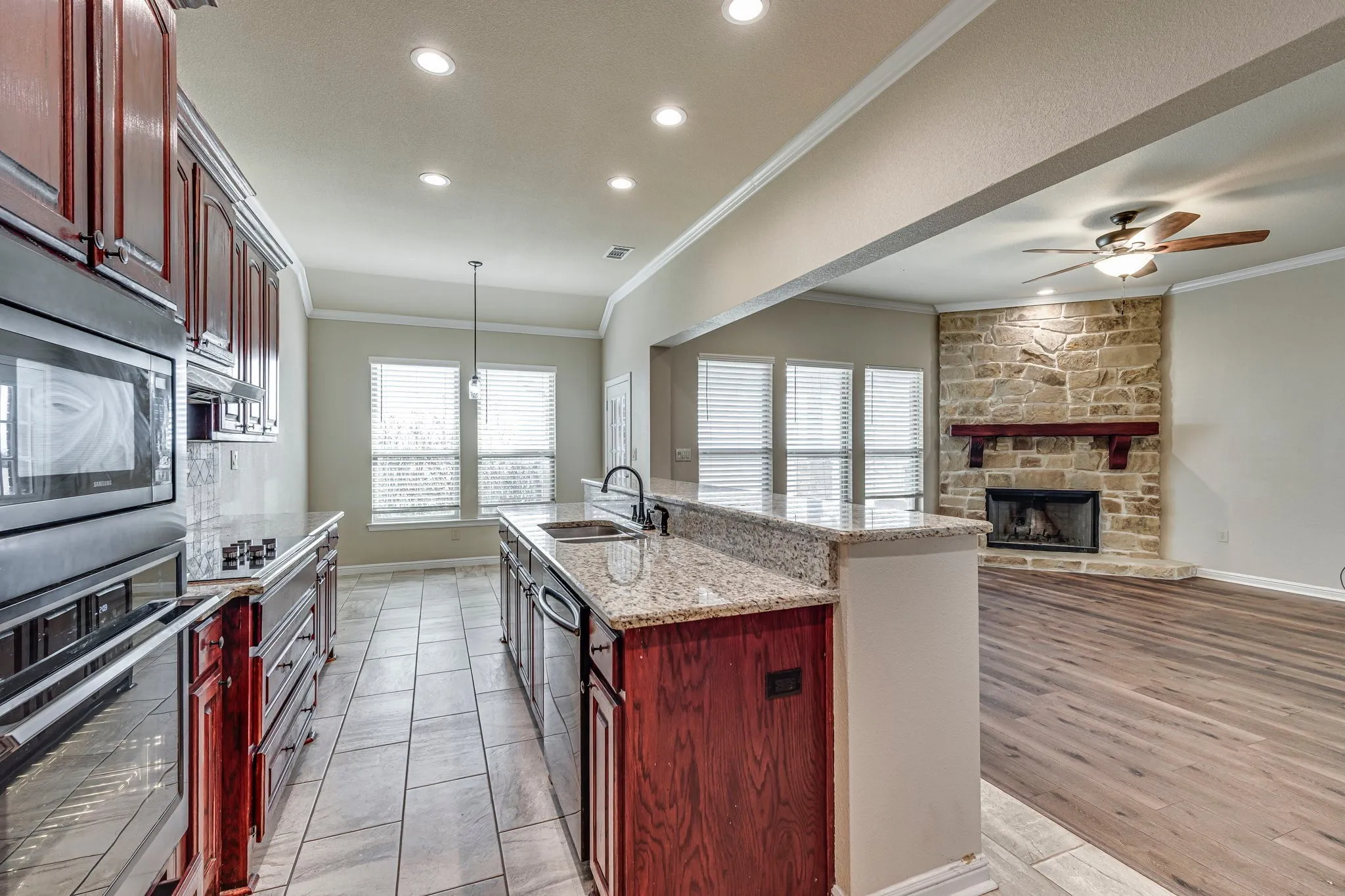 Kitchen featuring reddish brown cabinets, light stone countertops, stainless steel appliances, crown molding, and hanging light fixtures
