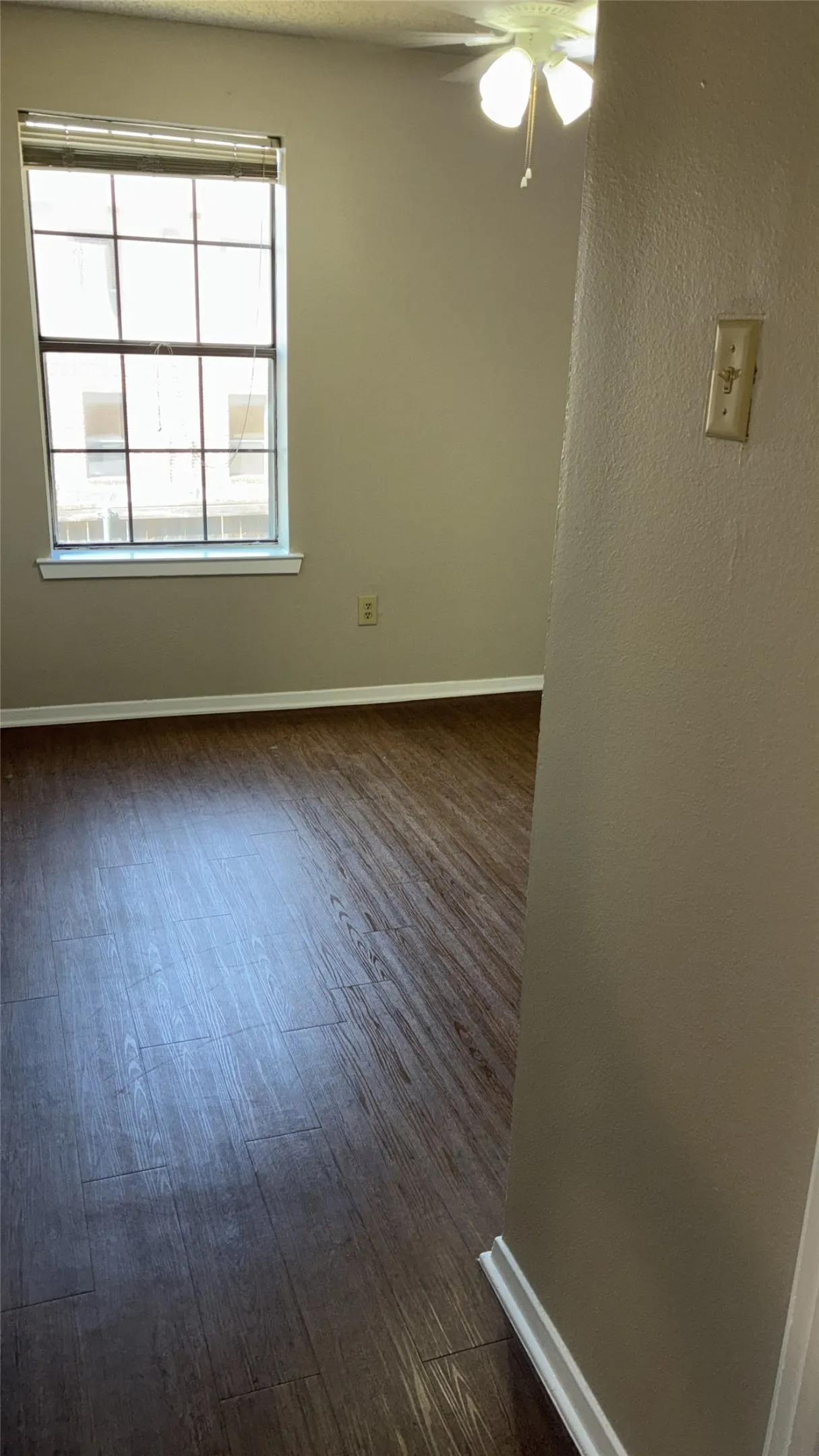 Recessed window with blinds, wood-finish flooring, ceiling fan with light fixture, and neutral wall paint