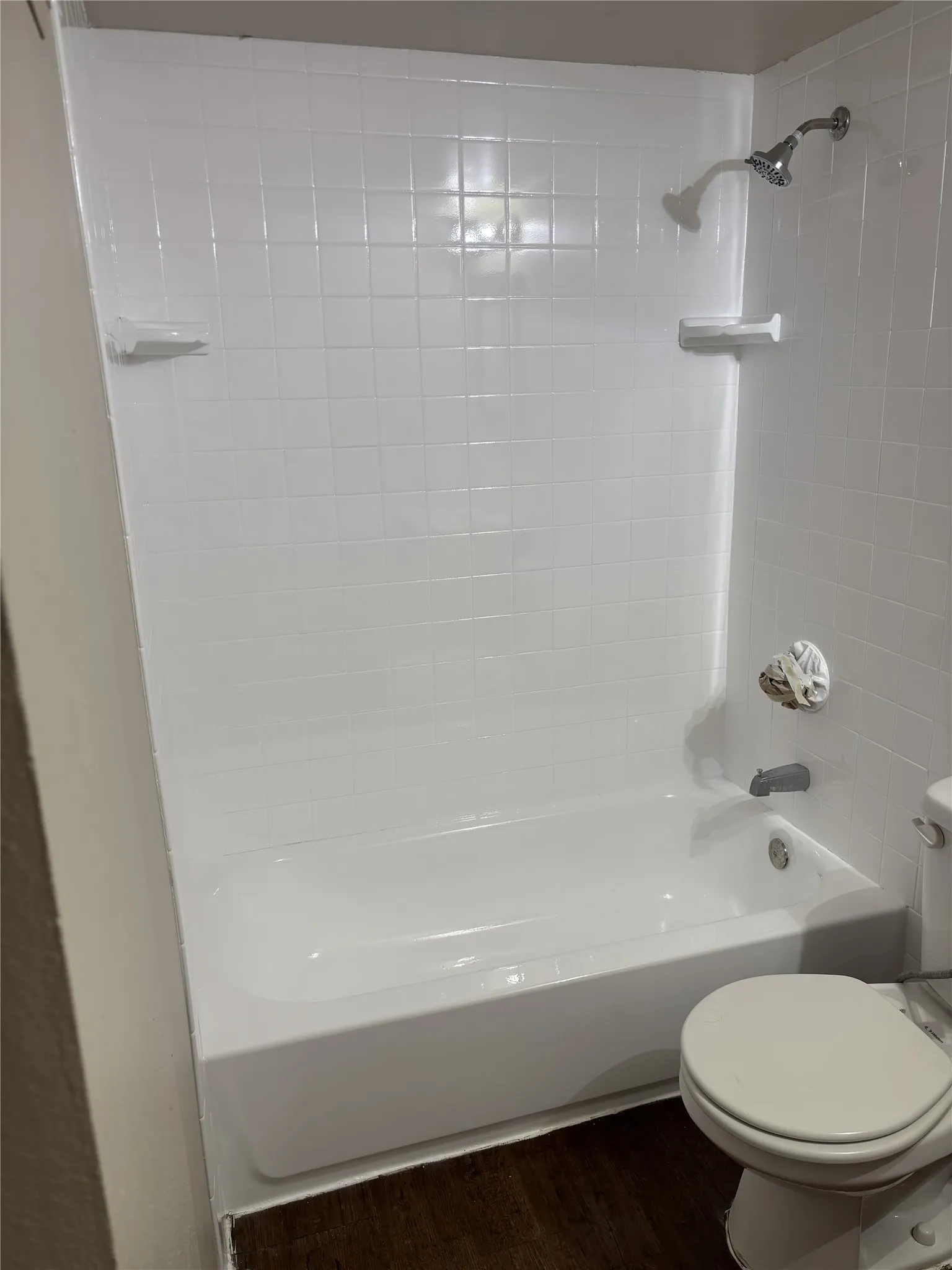 White tile shower surround with integrated soap dishes, chrome shower head, and built-in tub