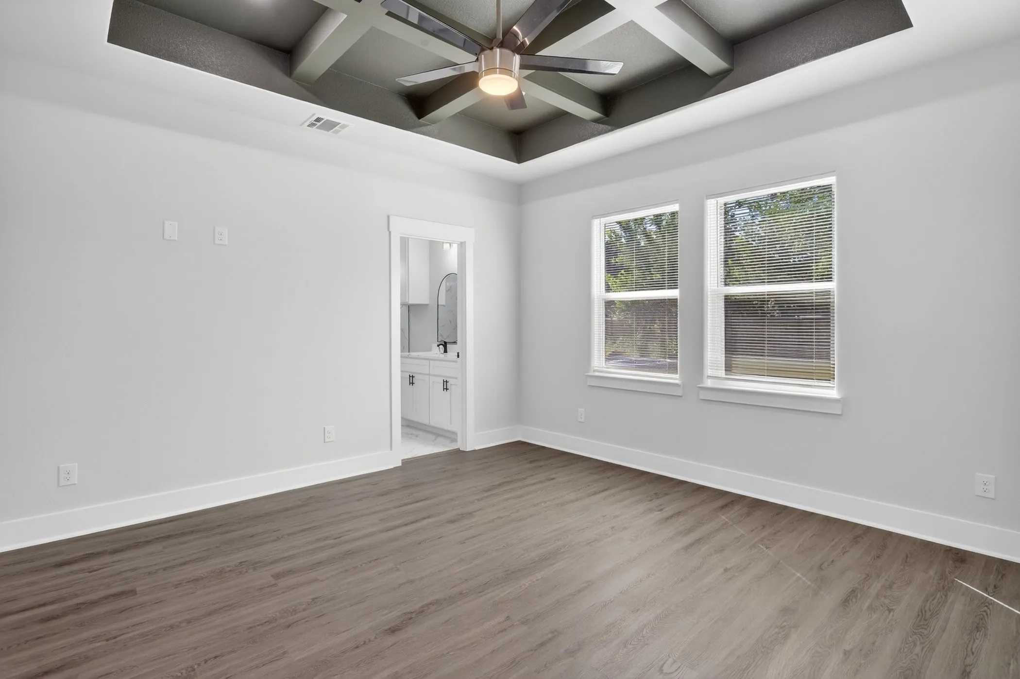 Wood-finish flooring throughout, featuring a tray ceiling with exposed beams and a ceiling fan