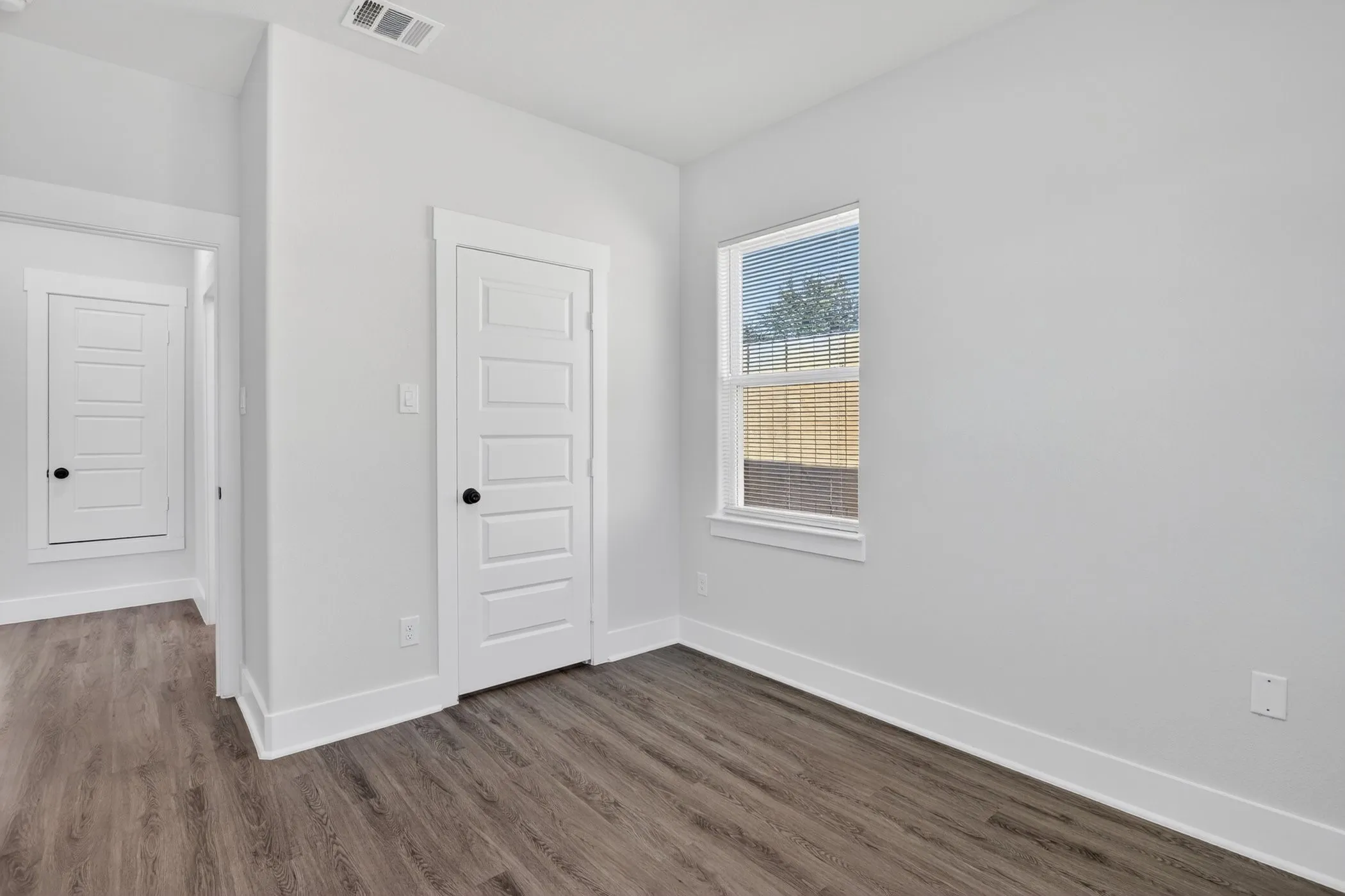 Interior room featuring wood-finish flooring, white walls, and a window with blinds