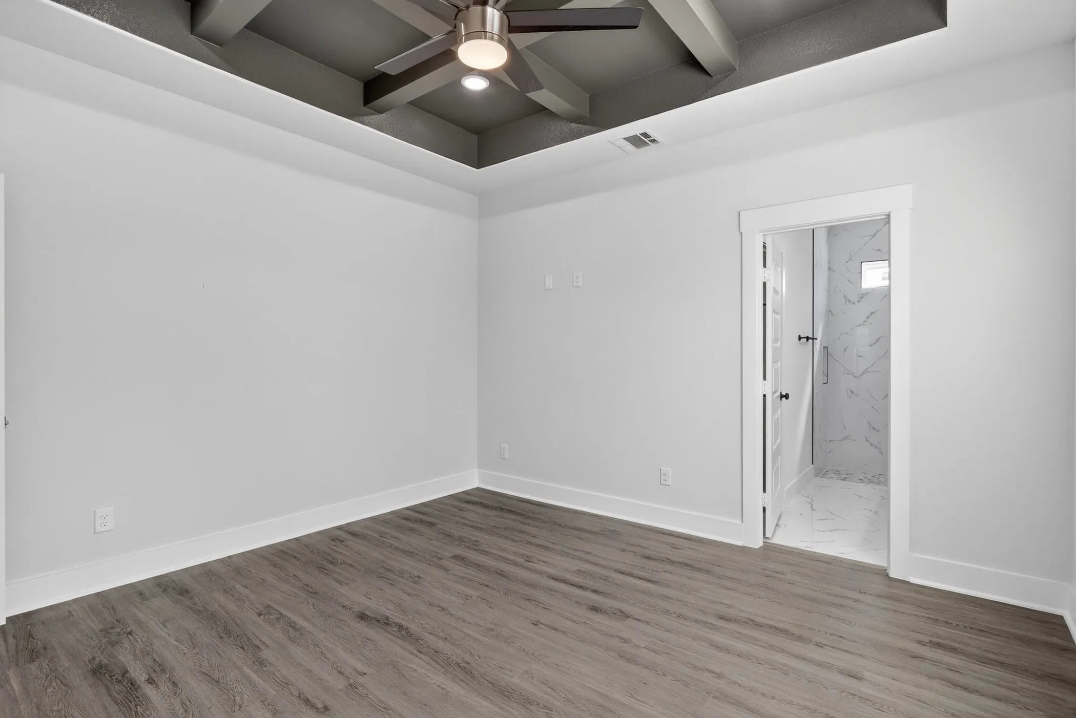 Room featuring wood-finish flooring, a tray ceiling with exposed beams, and a modern ceiling fan