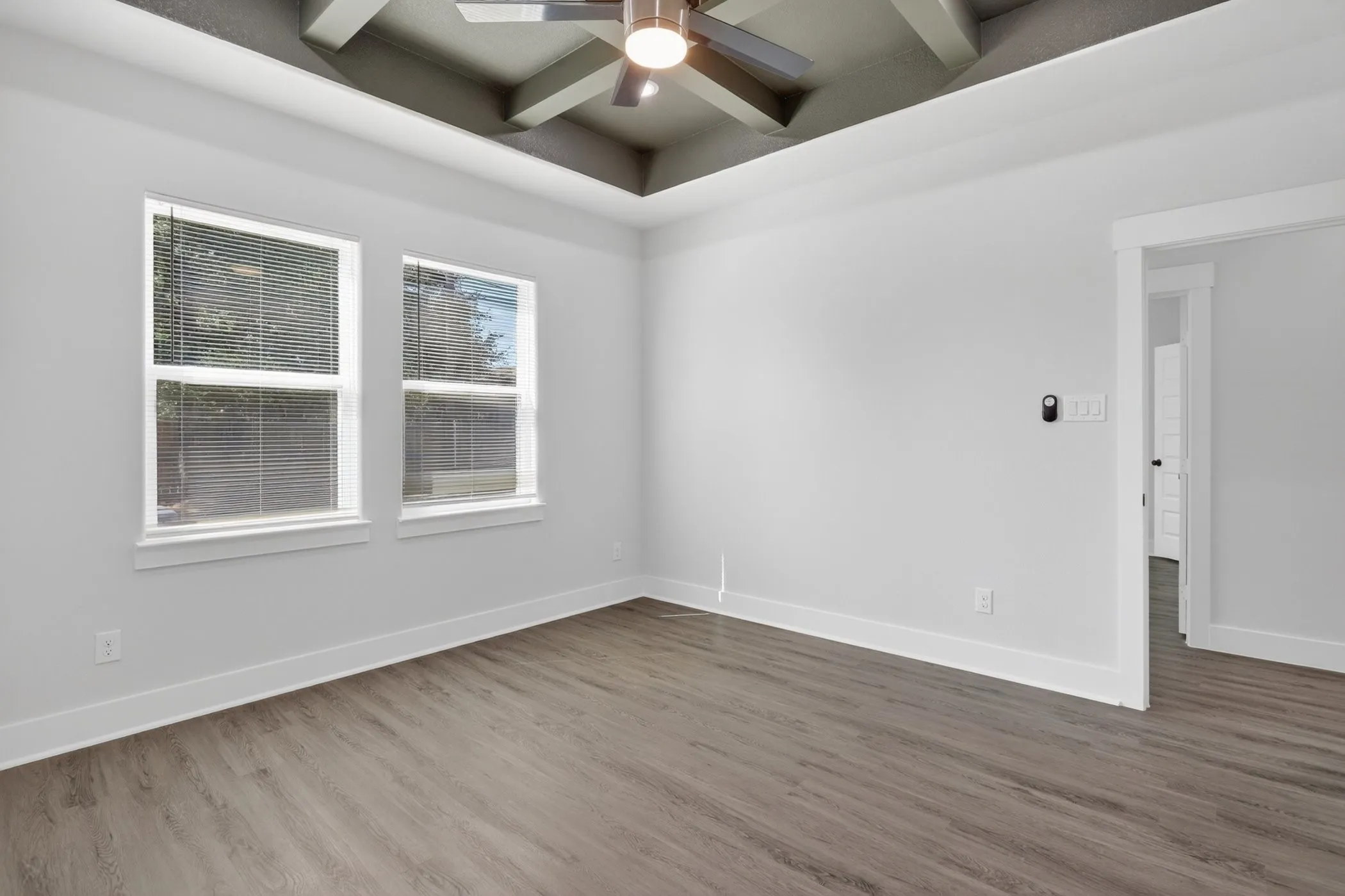 Spacious room featuring a decorative tray ceiling with a ceiling fan, two windows, wood-finish flooring, and crisp white baseboards