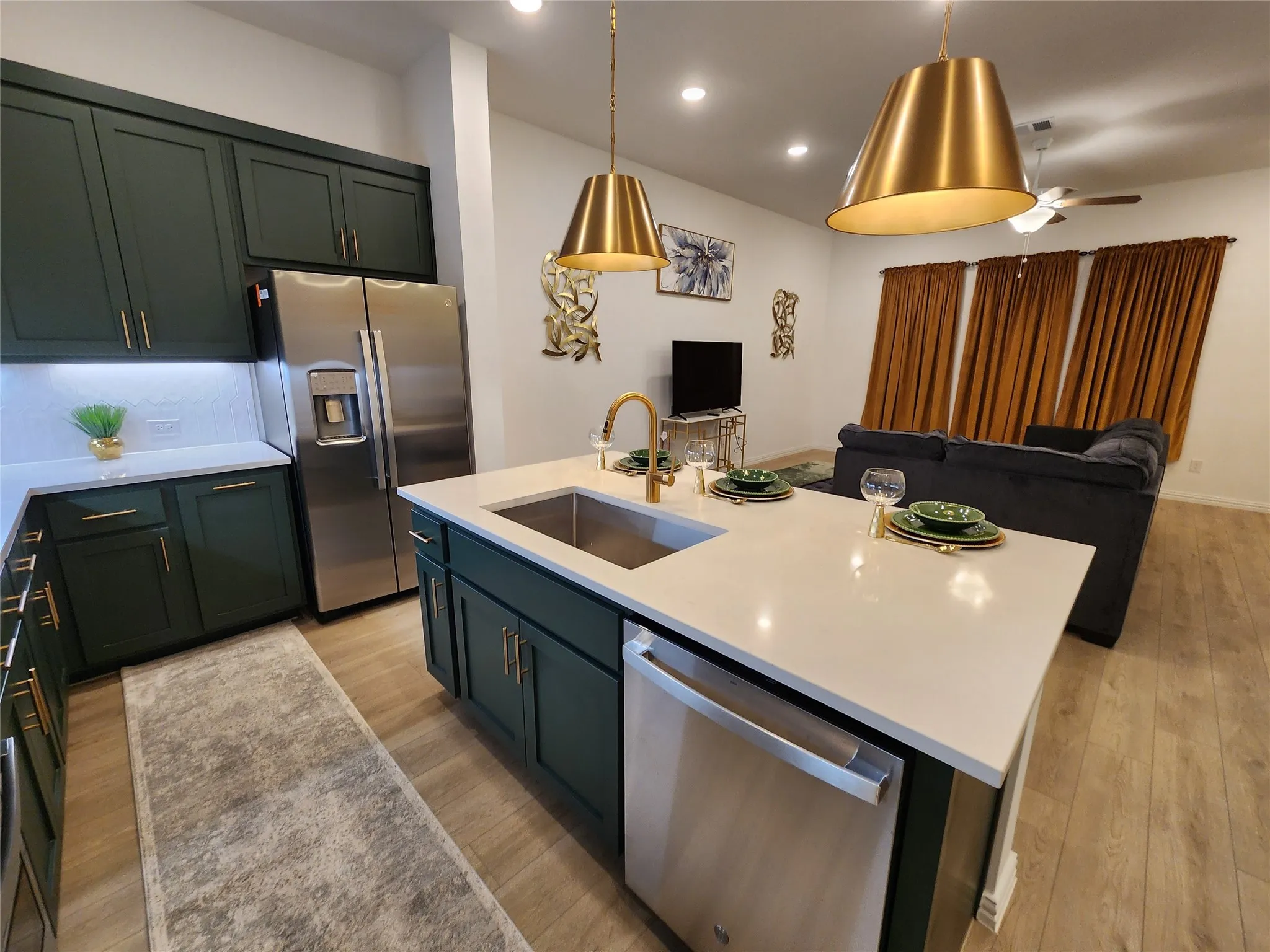 Kitchen featuring open floor plan, stainless steel appliances, decorative light fixtures, and a center island with sink