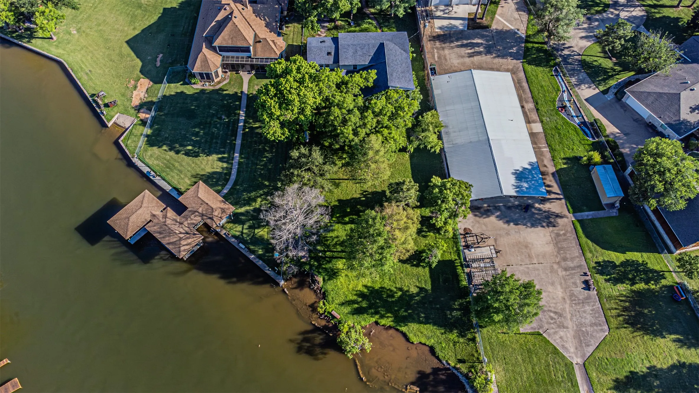 Waterfront property featuring a private boat dock with covered slips, substantial green space, and mature trees
