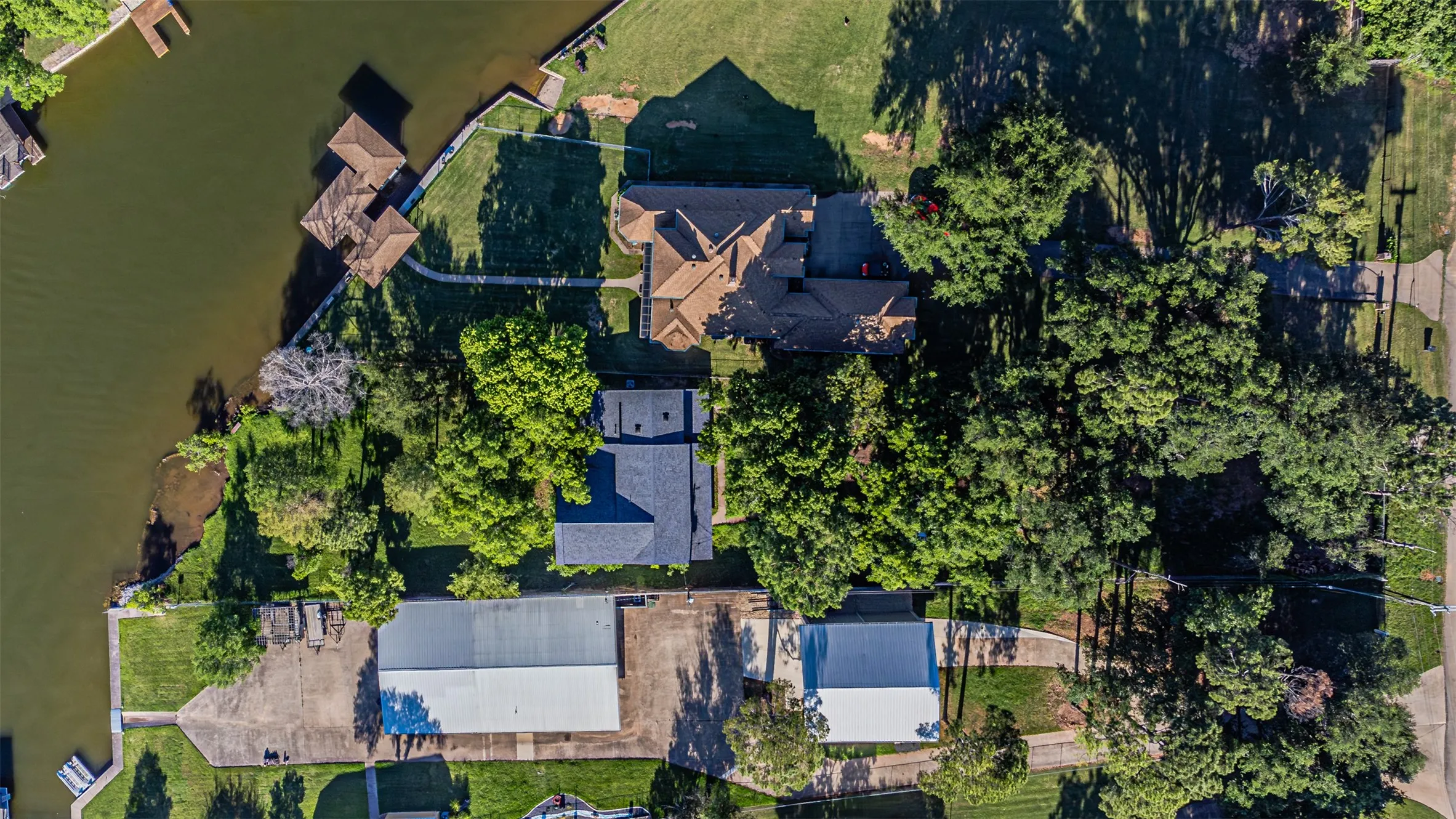 Waterfront property with extensive frontage, multiple boat docks, mature trees, and a large metal outbuilding