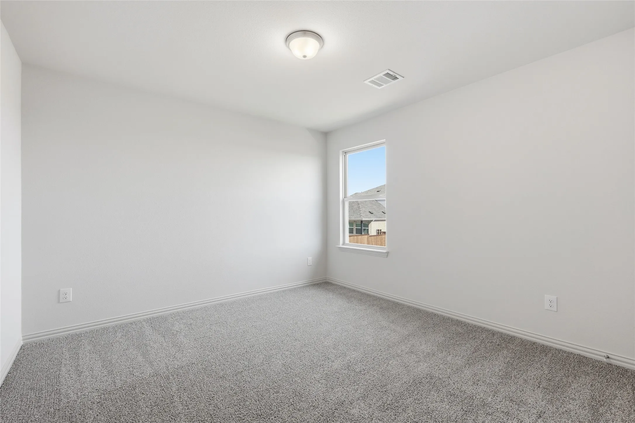 Bright room featuring neutral gray carpet, white painted walls, a single window, and a flush-mount ceiling light fixture