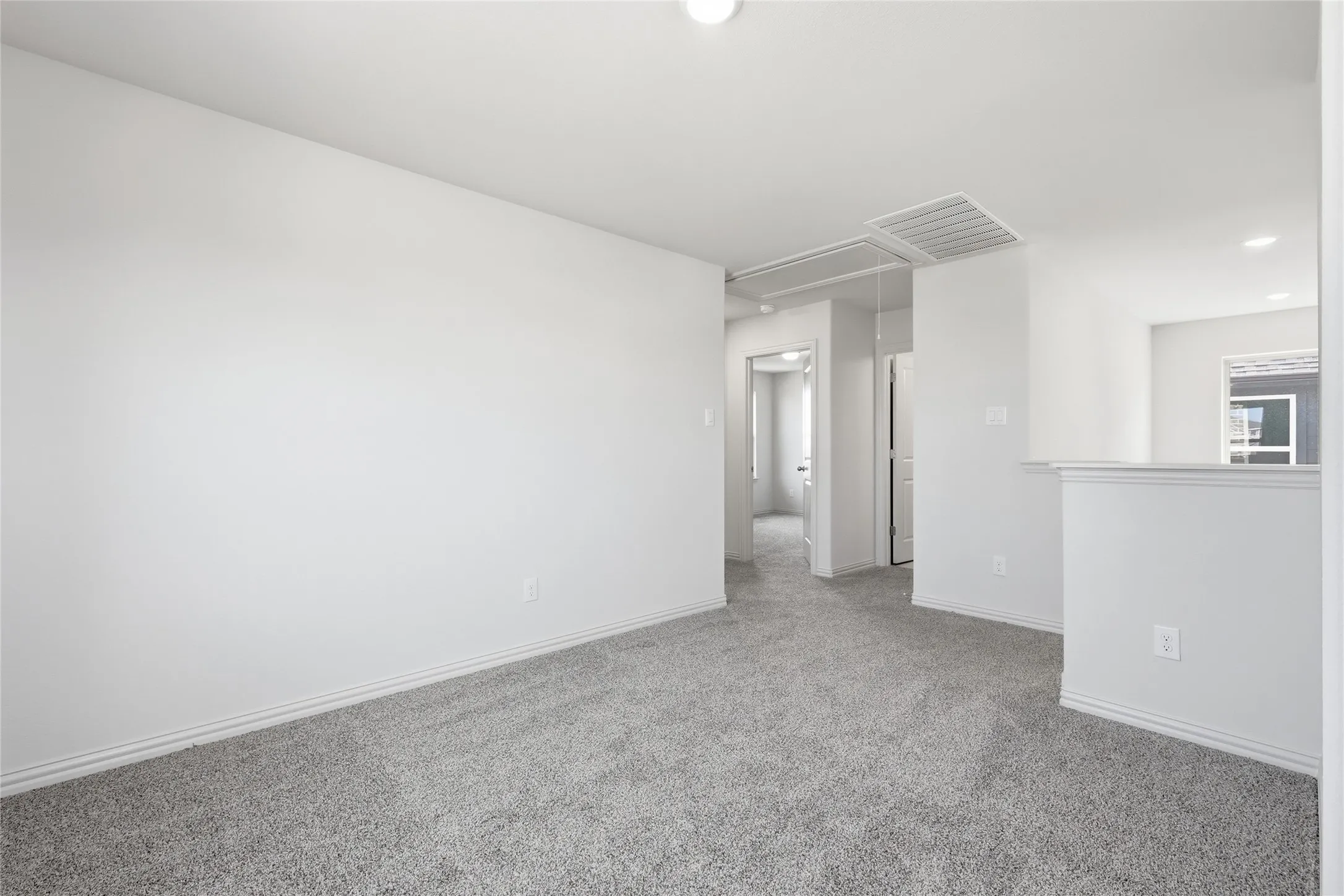 Spacious room featuring light gray carpeting, white walls, white baseboards, and overhead lighting