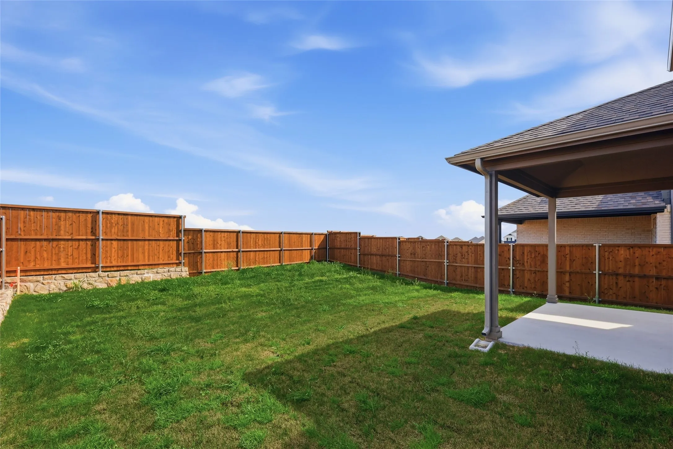 Expansive backyard featuring a manicured lawn, a full wood privacy fence, and a stone retaining wall