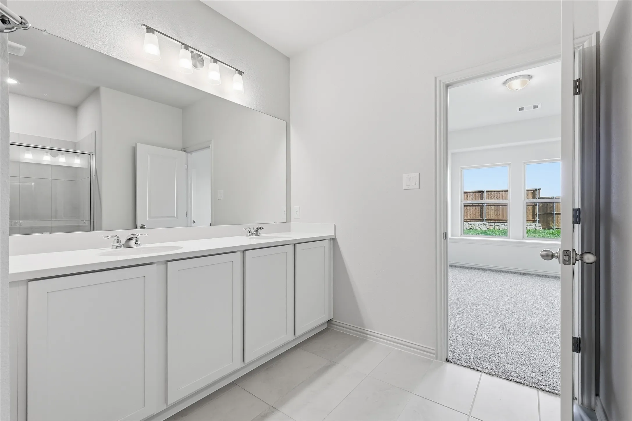 Dual vanity with white cabinetry and integrated sinks set beneath a large mirror with overhead lighting