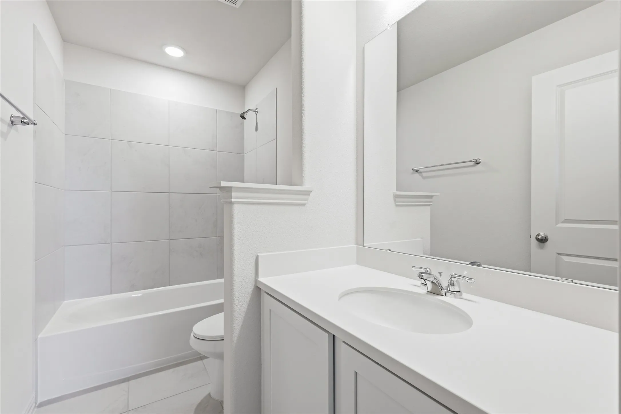 Contemporary bathroom featuring a tub/shower combination with large format tiled surround, a built-in vanity with an integrated sink, and a framed mirror