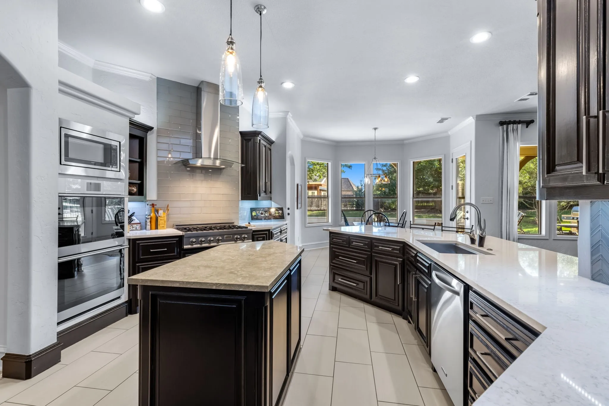 Kitchen with ornamental molding, tasteful backsplash, hanging light fixtures, light stone counters, and a center island