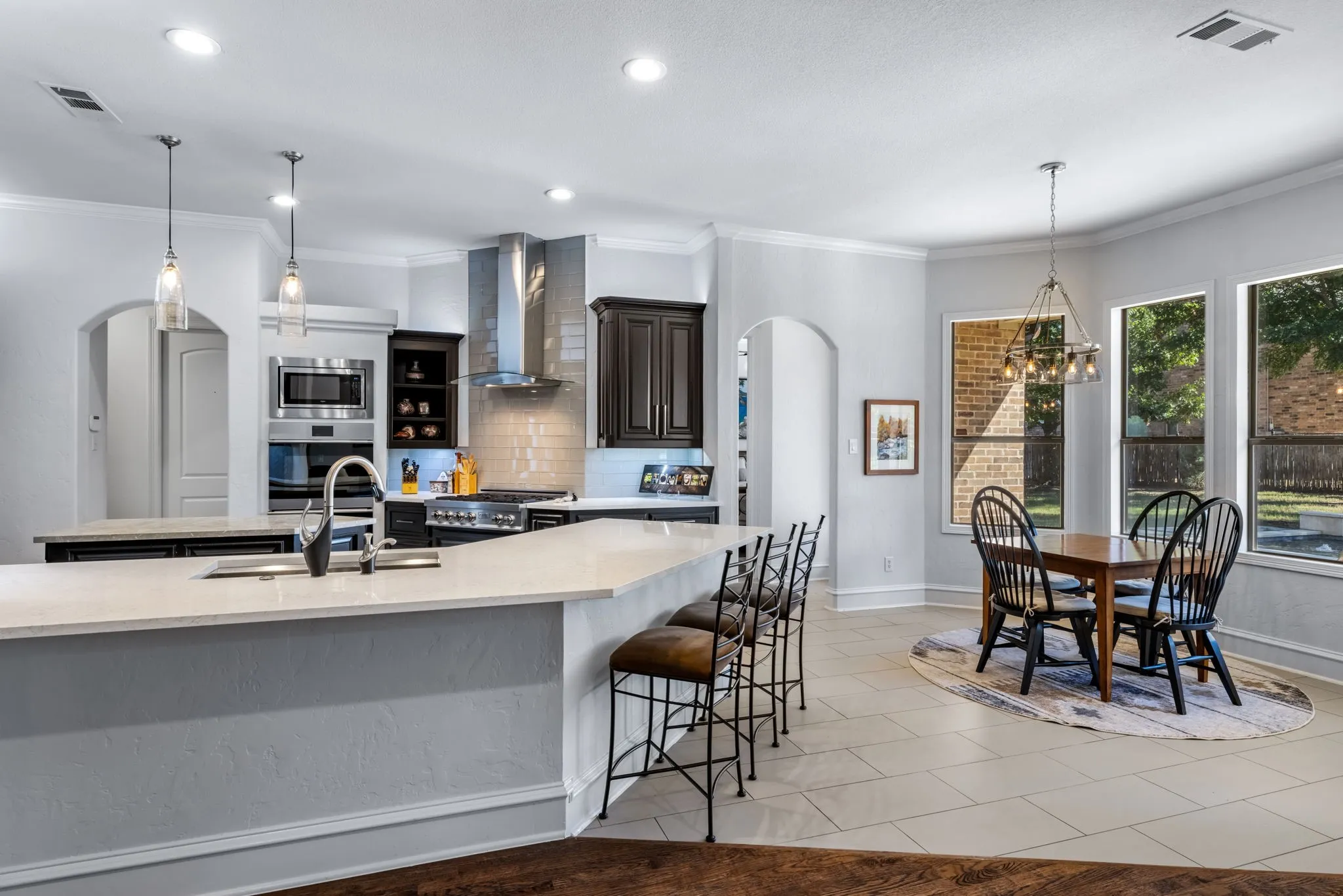 Kitchen with arched walkways, backsplash, decorative light fixtures, light tile patterned floors, and crown molding