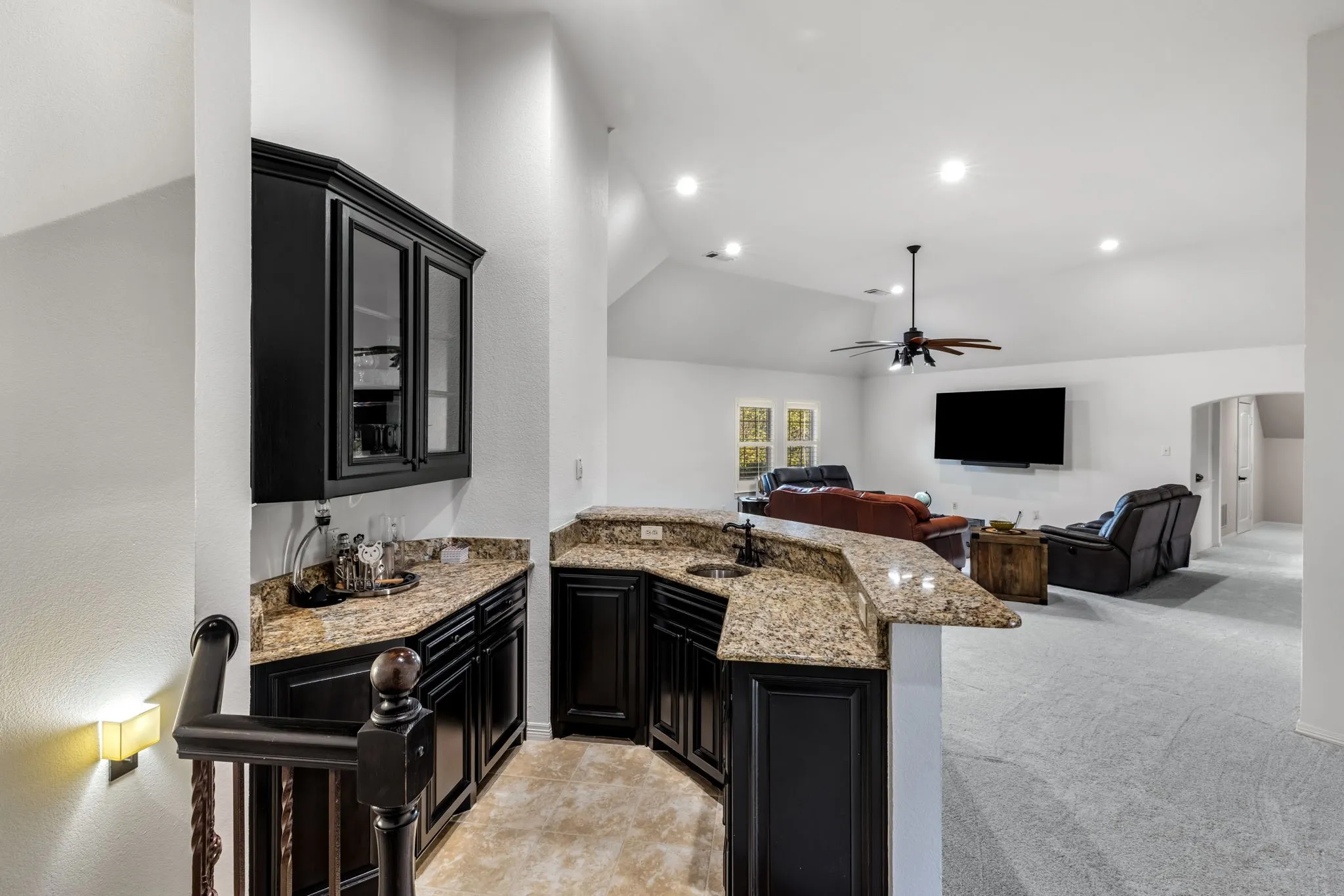 Kitchen featuring dark cabinets, light stone countertops, a peninsula, vaulted ceiling, and light colored carpet