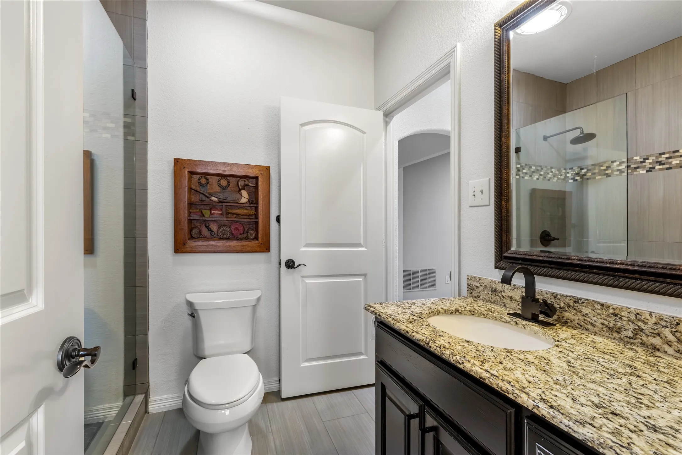 Bathroom with tiled shower, vanity, and a textured wall