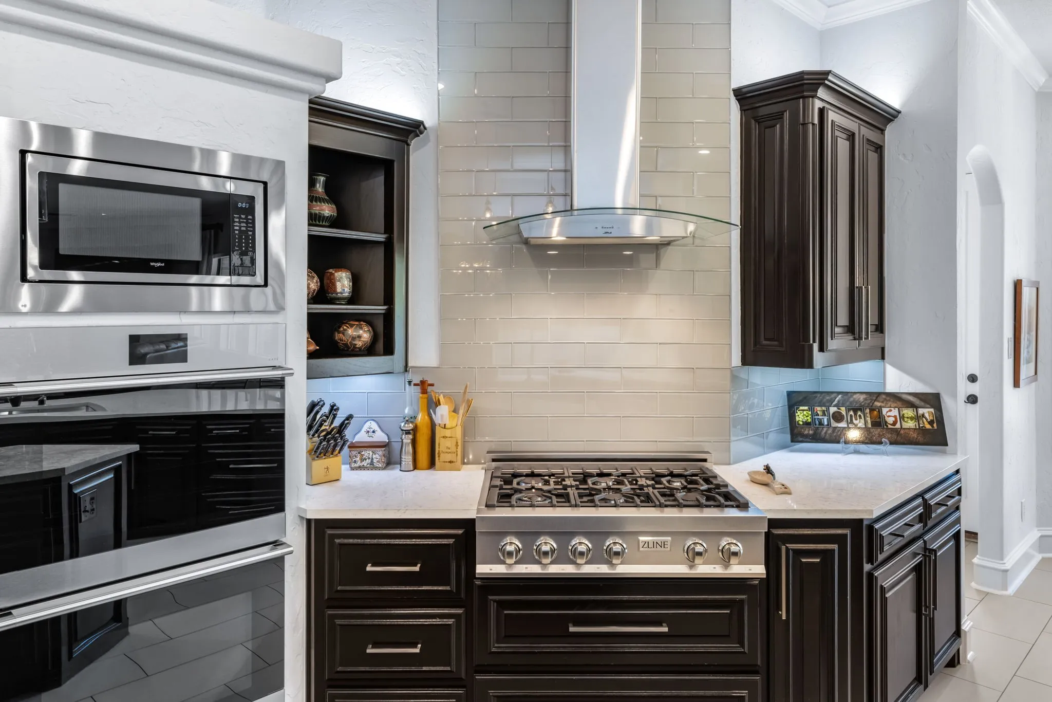 Kitchen with island exhaust hood, stainless steel appliances, light tile patterned floors, backsplash, and ornamental molding