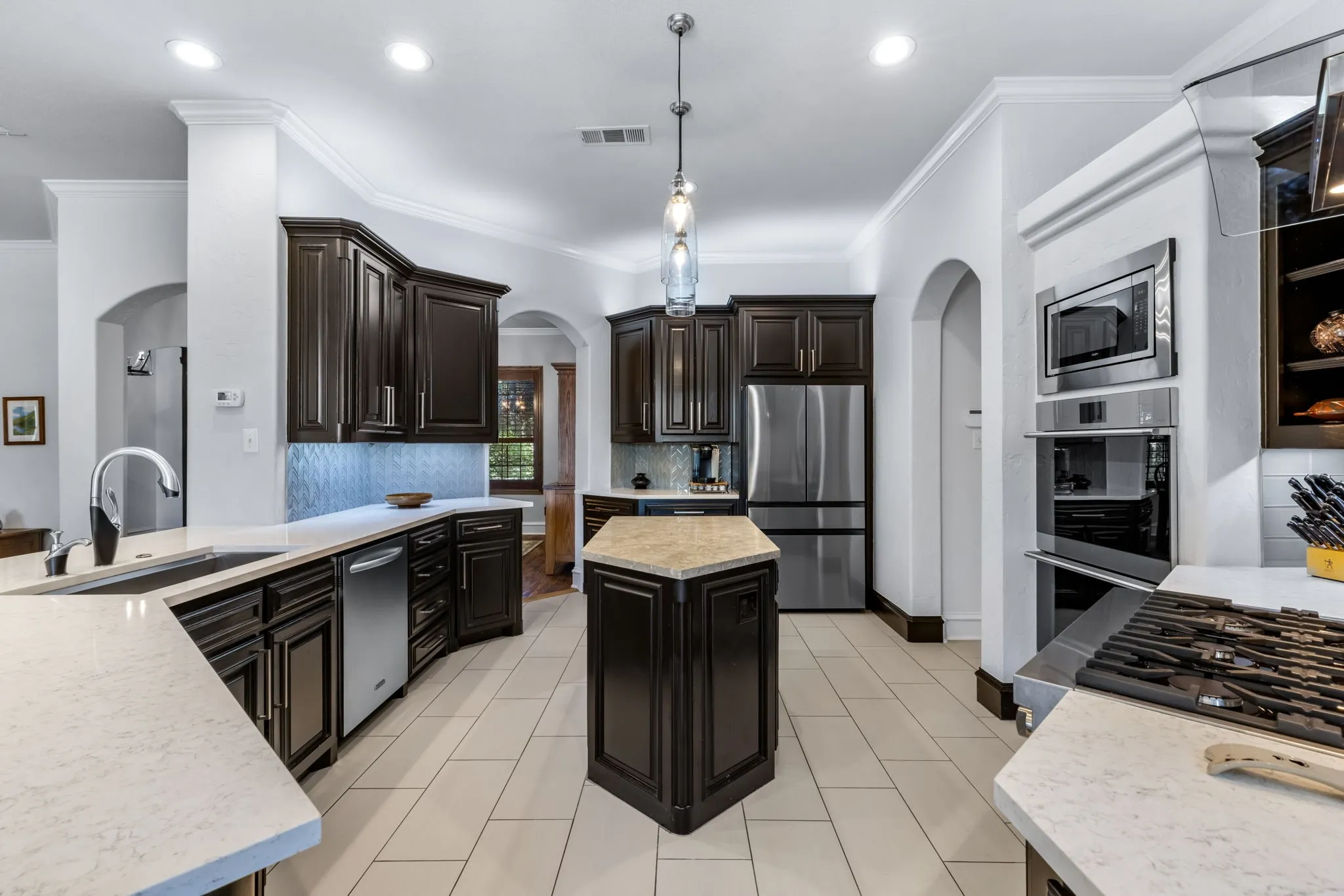 Kitchen with ornamental molding, a kitchen island, stainless steel appliances, backsplash, and arched walkways