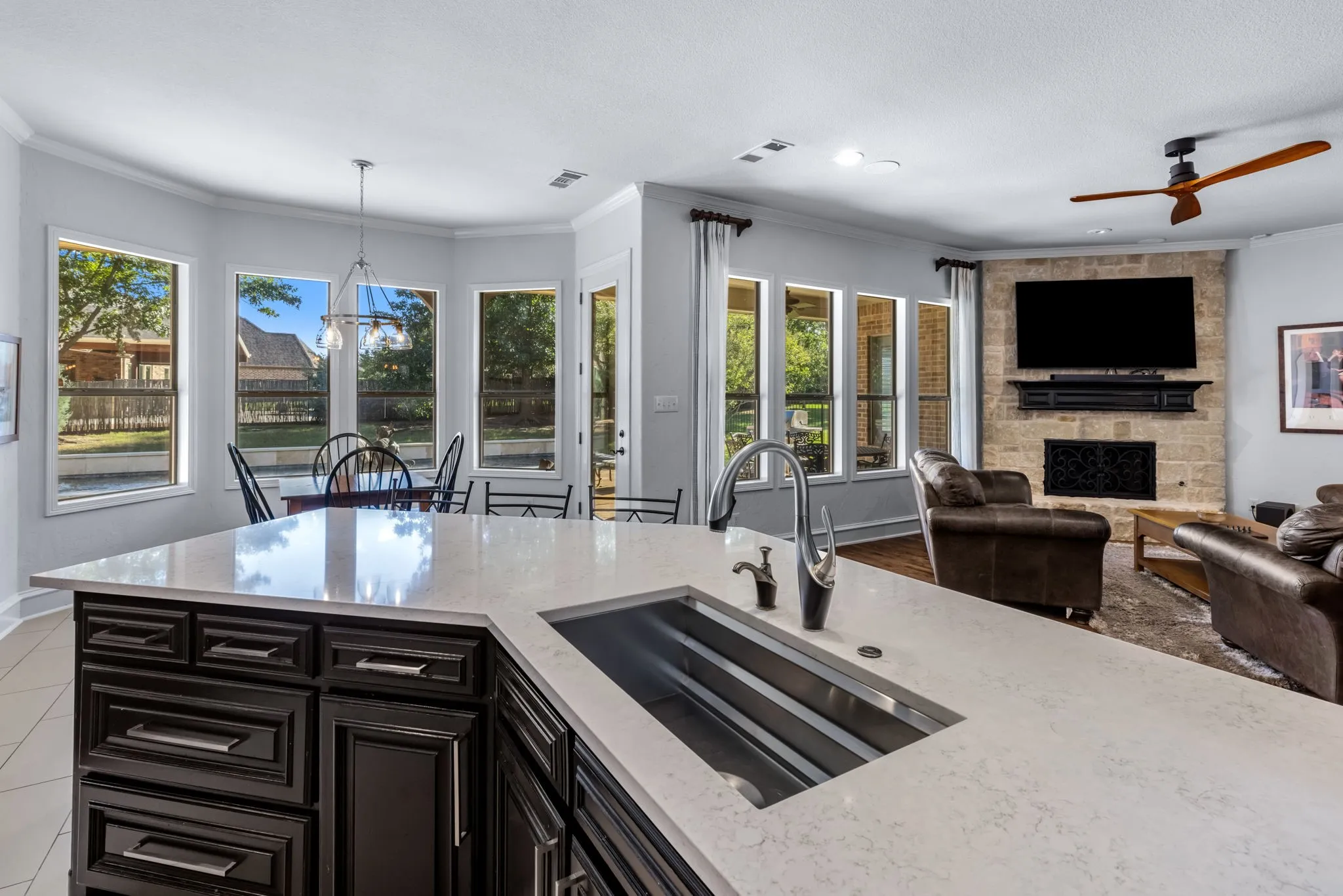 Kitchen with a fireplace, crown molding, dark cabinetry, light stone counters, and decorative light fixtures