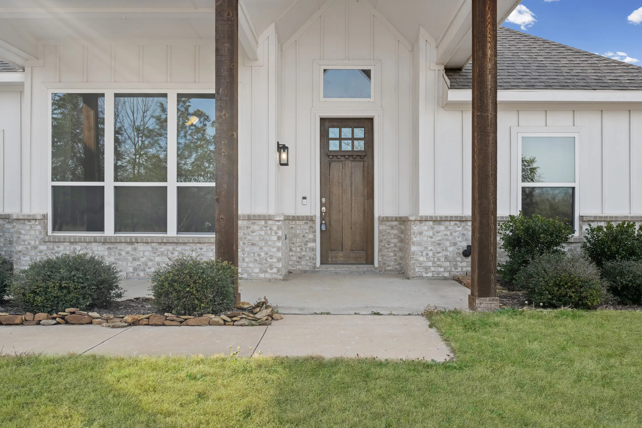Stained wood columns frame a warm, rustic front door with decorative glass, creating a striking focal point.